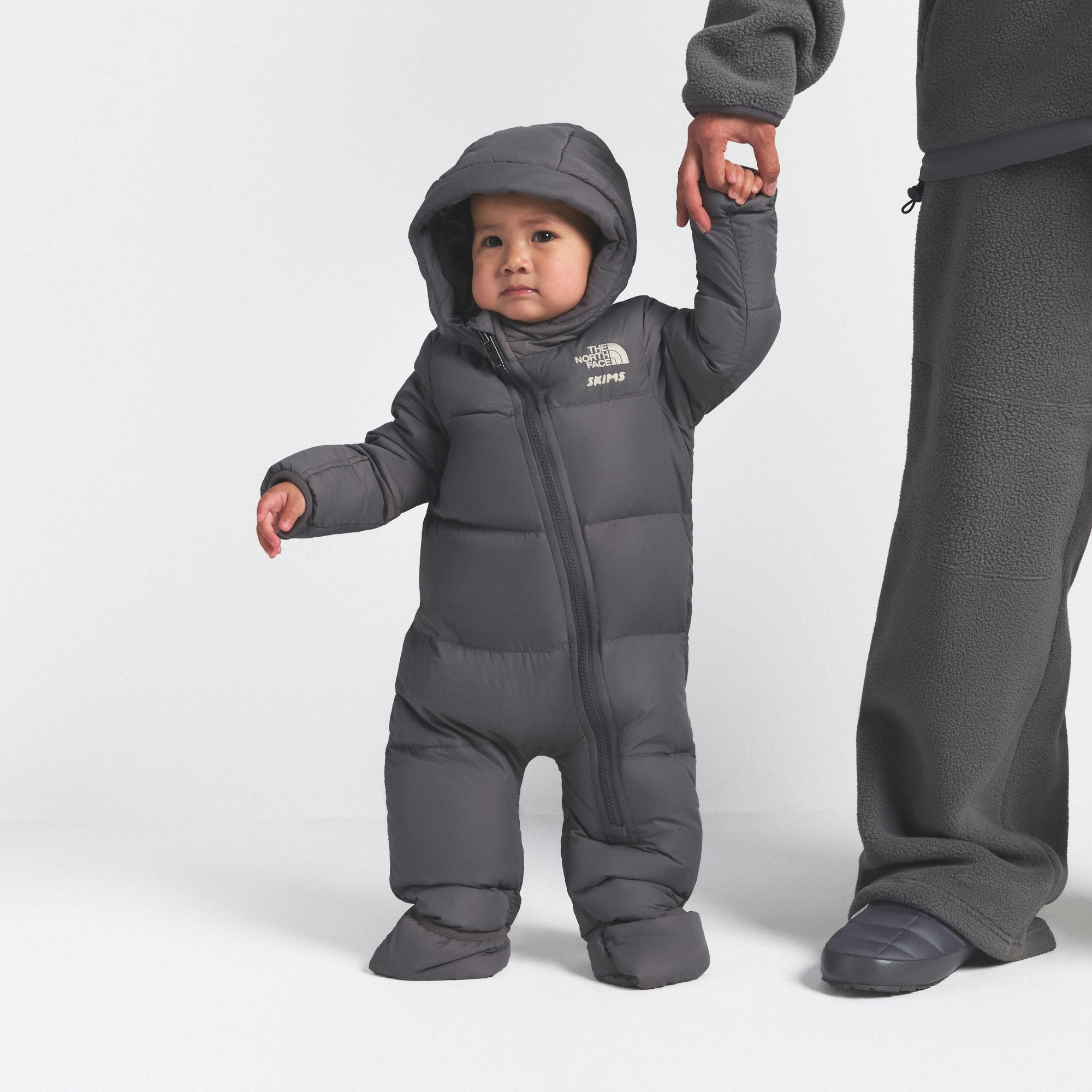 THE NORTH FACE X SKIMS BABY 1996 NUPTSE ONE-PIECE | GUNMETAL ON A MODEL FRONT VIEW @ | FOCUS: 0.0, 1.0, 0.9