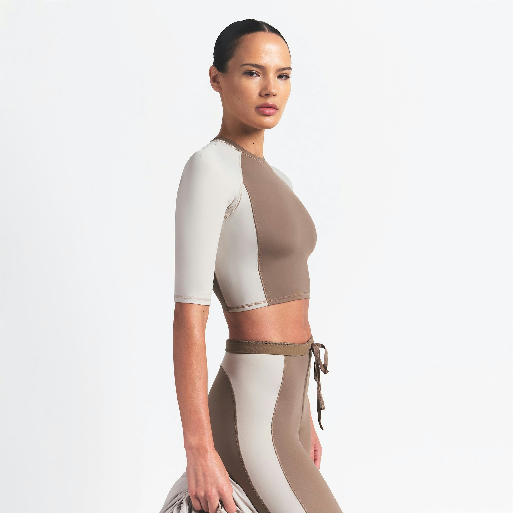 NikeSKIMS SHINE PADDED HALF SLEEVE CROP TOP | TRUFFLE AND STONE ON A MODEL SIDE VIEW @ | FOCUS: 0.0, 1.0, 0.9