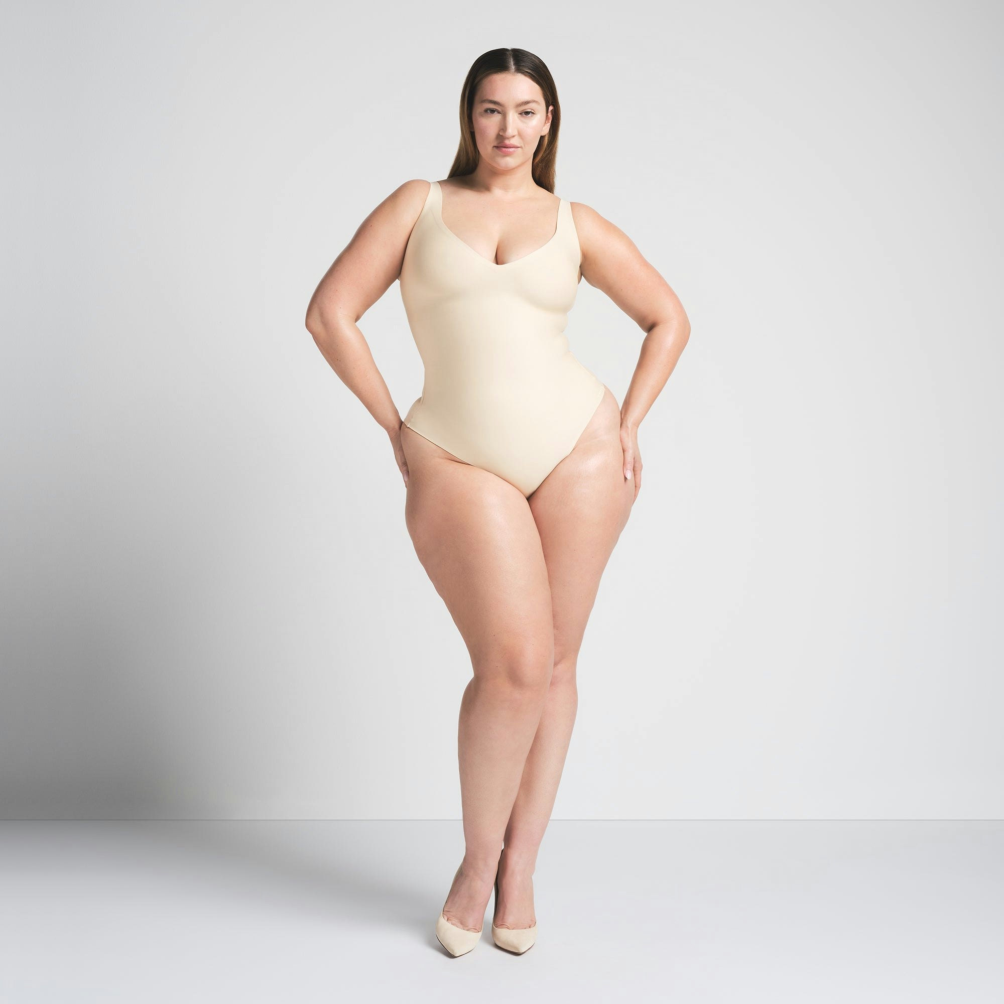 SKIMS BODY UNLINED PLUNGE THONG BODYSUIT | SAND ON A MODEL FRONT VIEW @ | FOCUS: 0.0, 1.0, 0.9