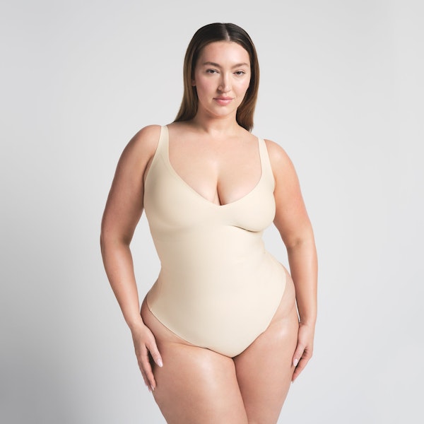 SKIMS BODY UNLINED PLUNGE THONG BODYSUIT | SAND ON A MODEL FRONT VIEW @ | FOCUS: 0.0, 1.0, 0.9