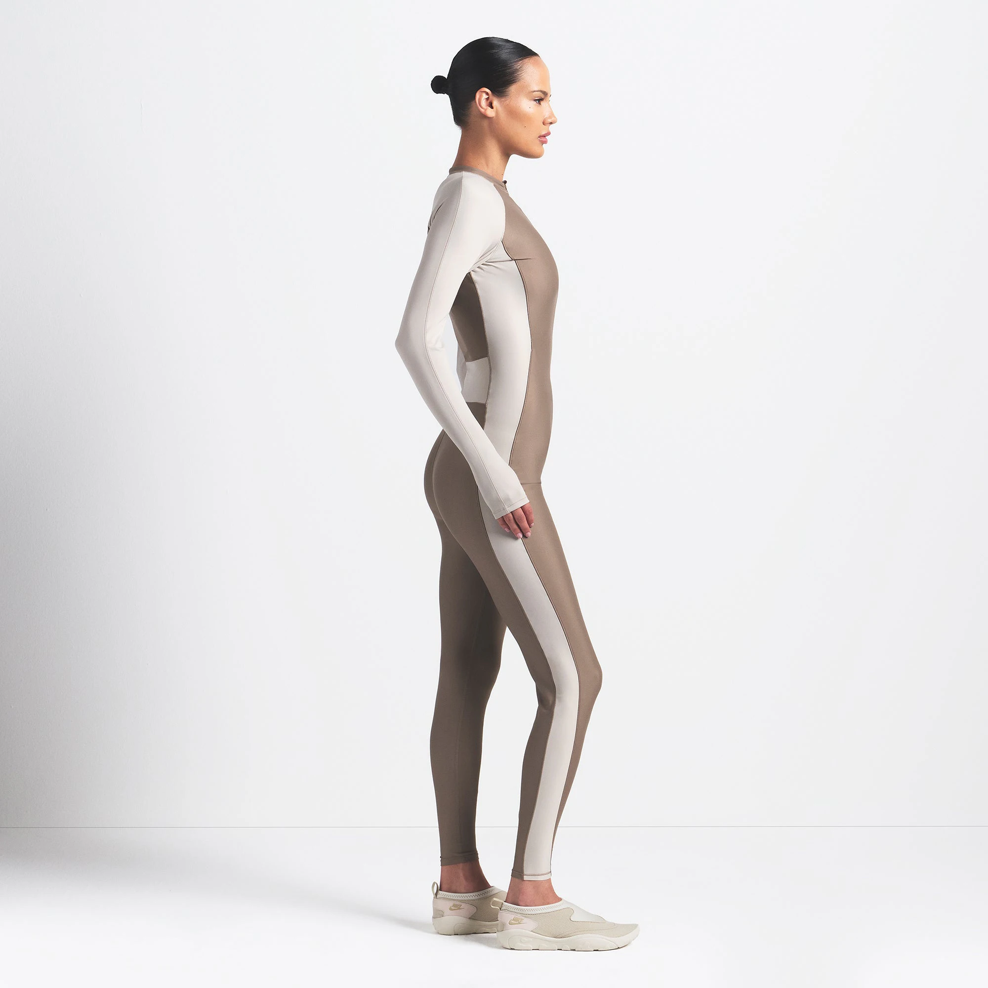 NikeSKIMS SHINE ZIP FRONT LONG ONESIE | TRUFFLE AND STONE ON A MODEL SIDE VIEW @ | FOCUS: 0.0, 1.0, 0.9
