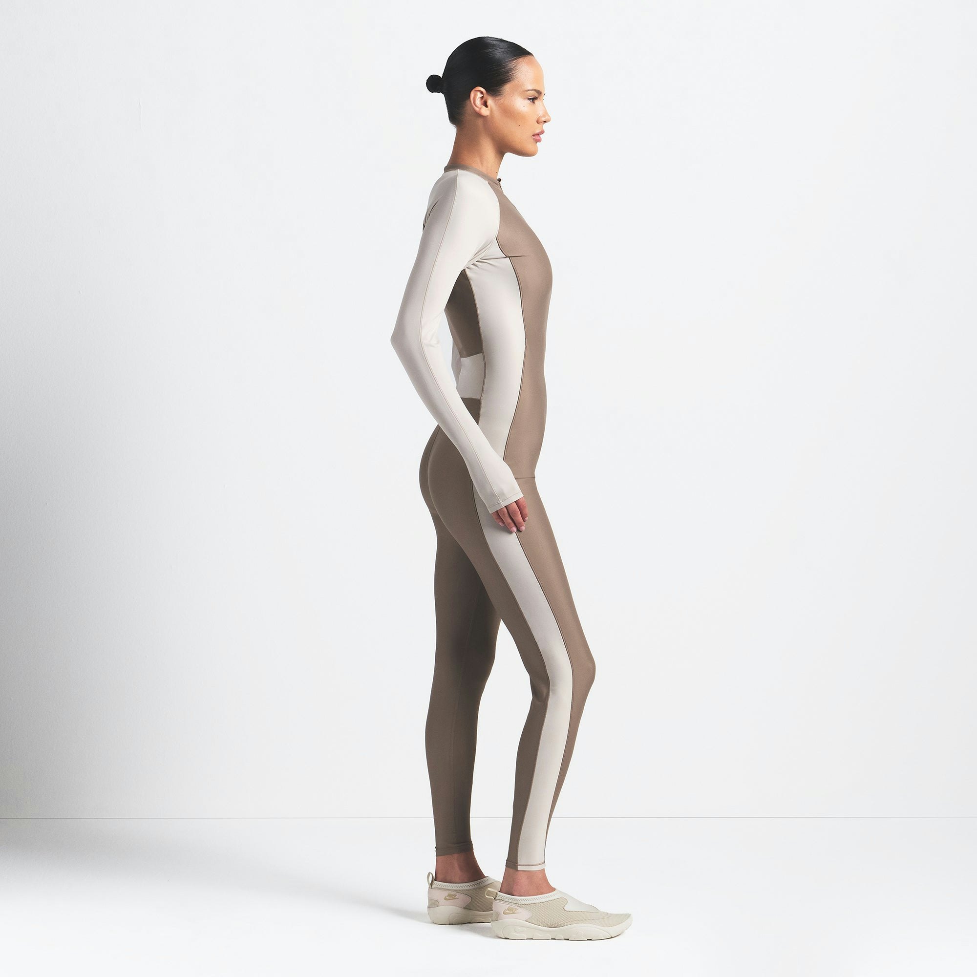 NikeSKIMS SHINE ZIP FRONT LONG ONESIE | TRUFFLE AND STONE ON A MODEL SIDE VIEW @ | FOCUS: 0.0, 1.0, 0.9