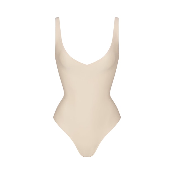 SKIMS BODY UNLINED PLUNGE THONG BODYSUIT | SAND (SHAPEWEAR BODYSUITS, SHAPEWEAR) LAYS FLAT ON A WHITE BACKGROUND | FLT