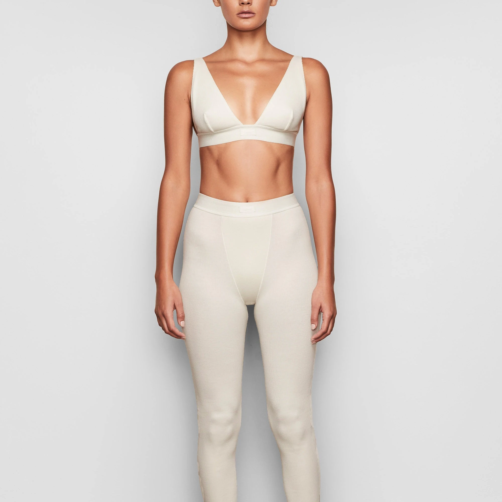 A MODEL STANDS FACING FORWARD WEARING THE SKIMS COTTON RIB LEGGING IN BONE 