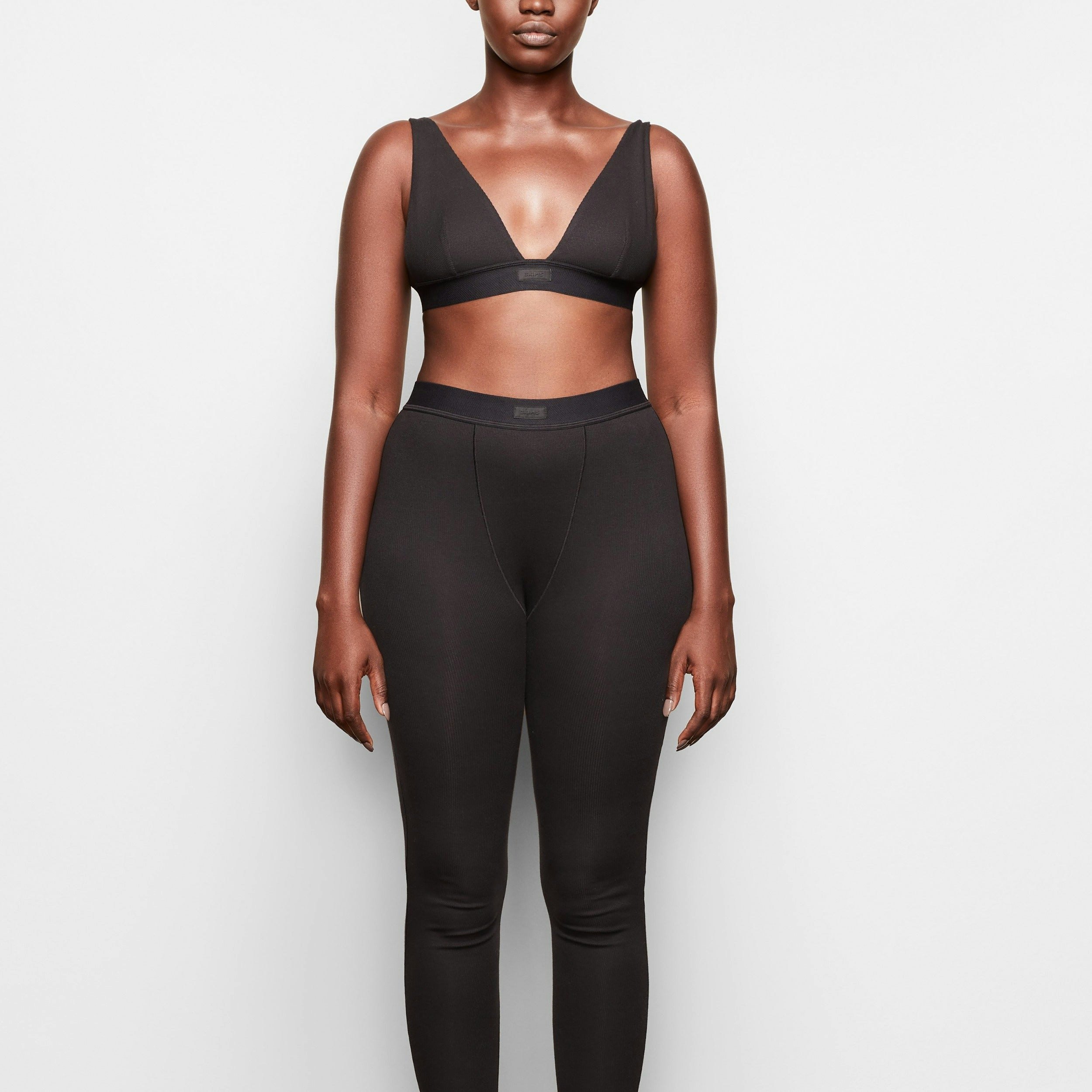 A MODEL STANDS FACING FORWARD WEARING THE SKIMS COTTON RIB LEGGING IN SOOT 