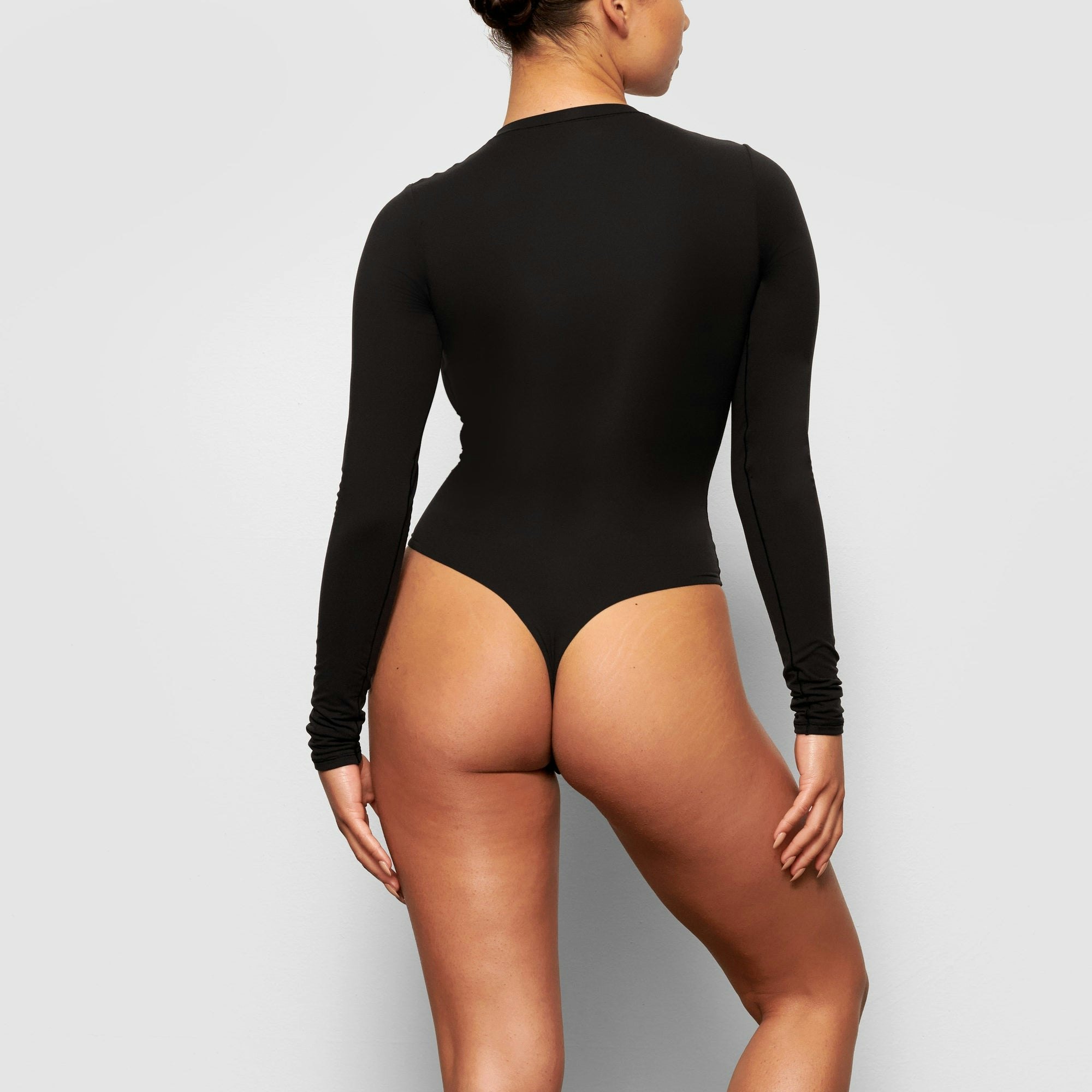 A MODEL STANDS WITH HER BACK TO THE CAMERA SHOWING THE FITS EVERYBODY LONG SLEEVE CREW NECK BODYSUIT | ONYX
