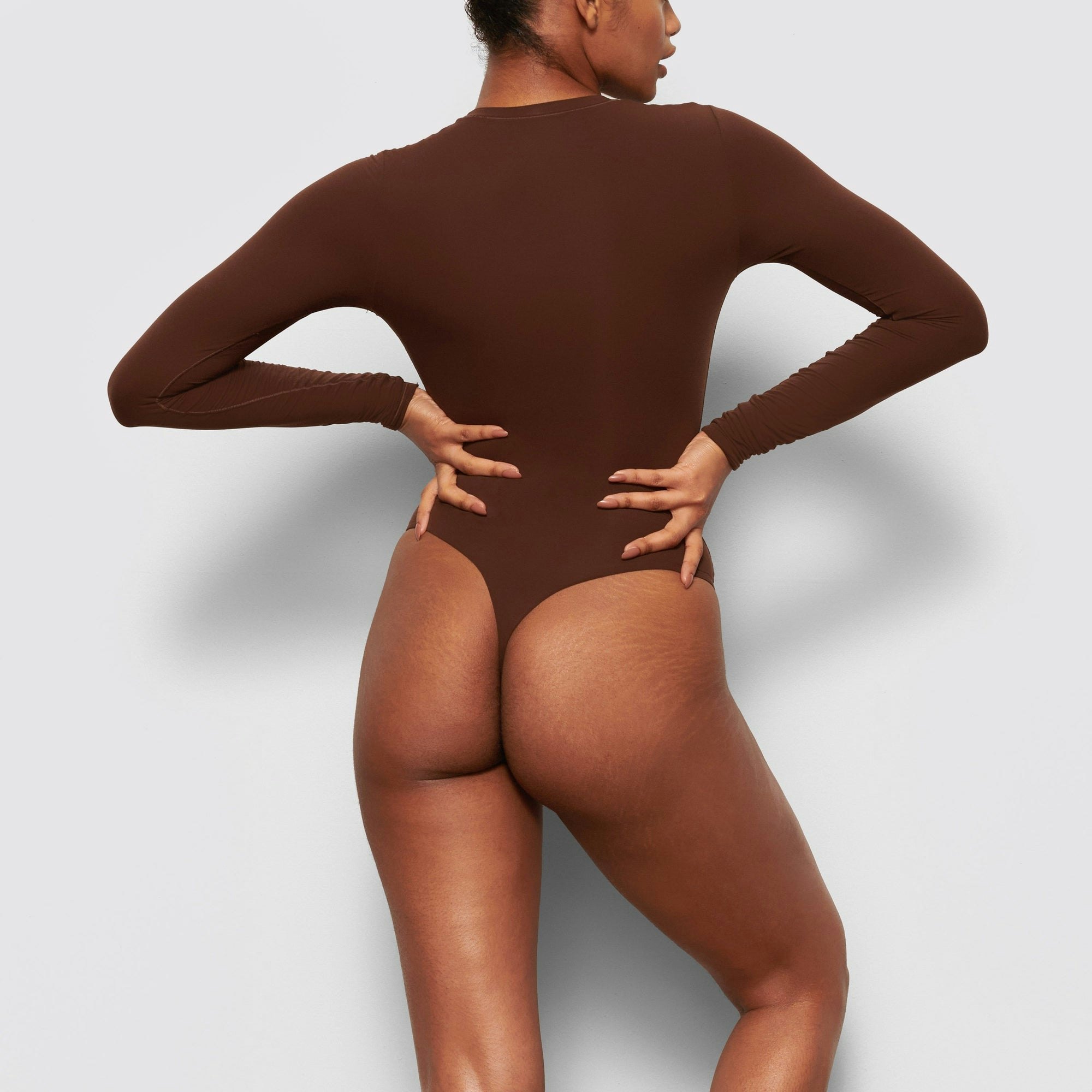 A MODEL STANDS WITH HER BACK TO THE CAMERA SHOWING THE FITS EVERYBODY LONG SLEEVE CREW NECK BODYSUIT | COCOA