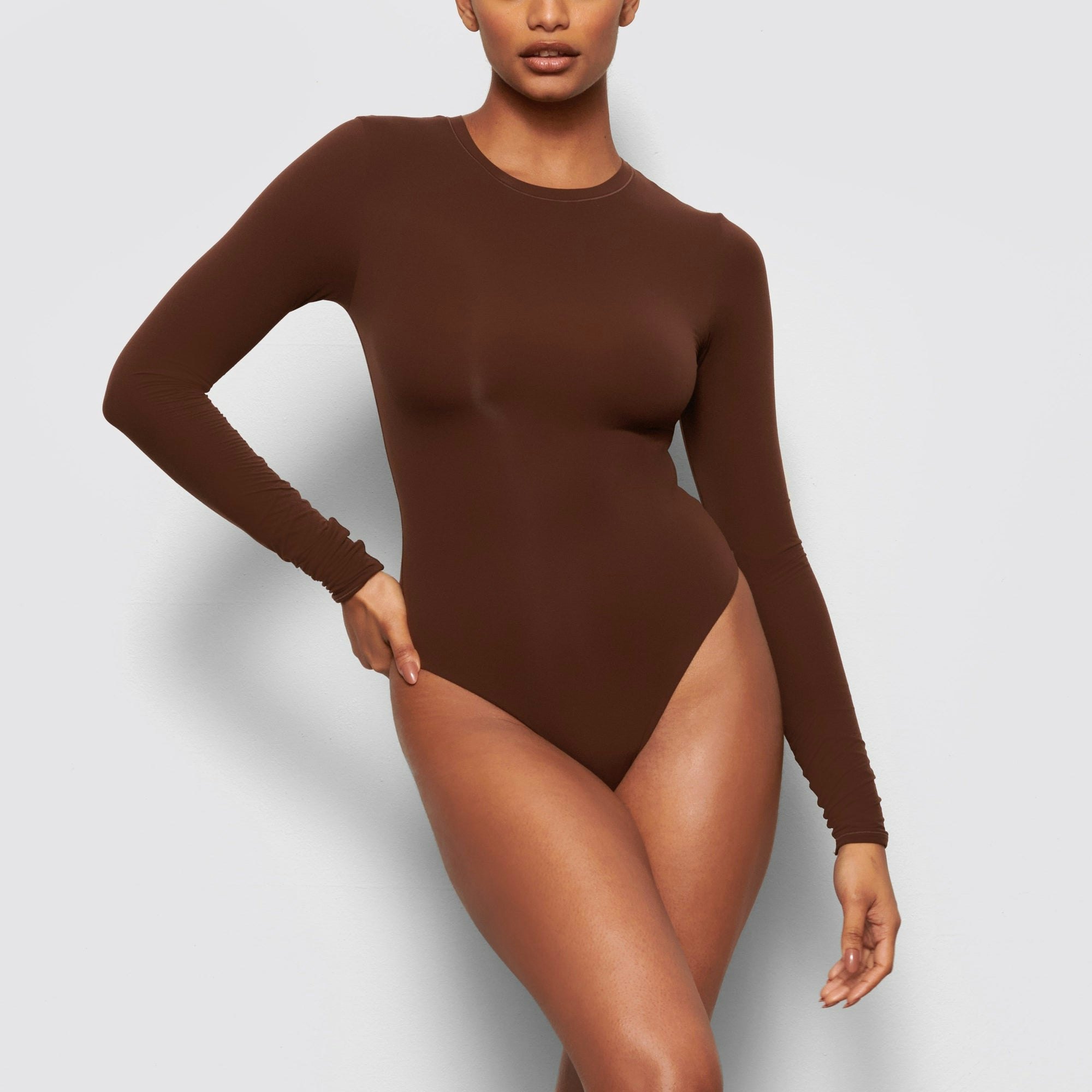 A MODEL STANDS FACING FORWARD WEARING THE FITS EVERYBODY LONG SLEEVE CREW NECK BODYSUIT | COCOA