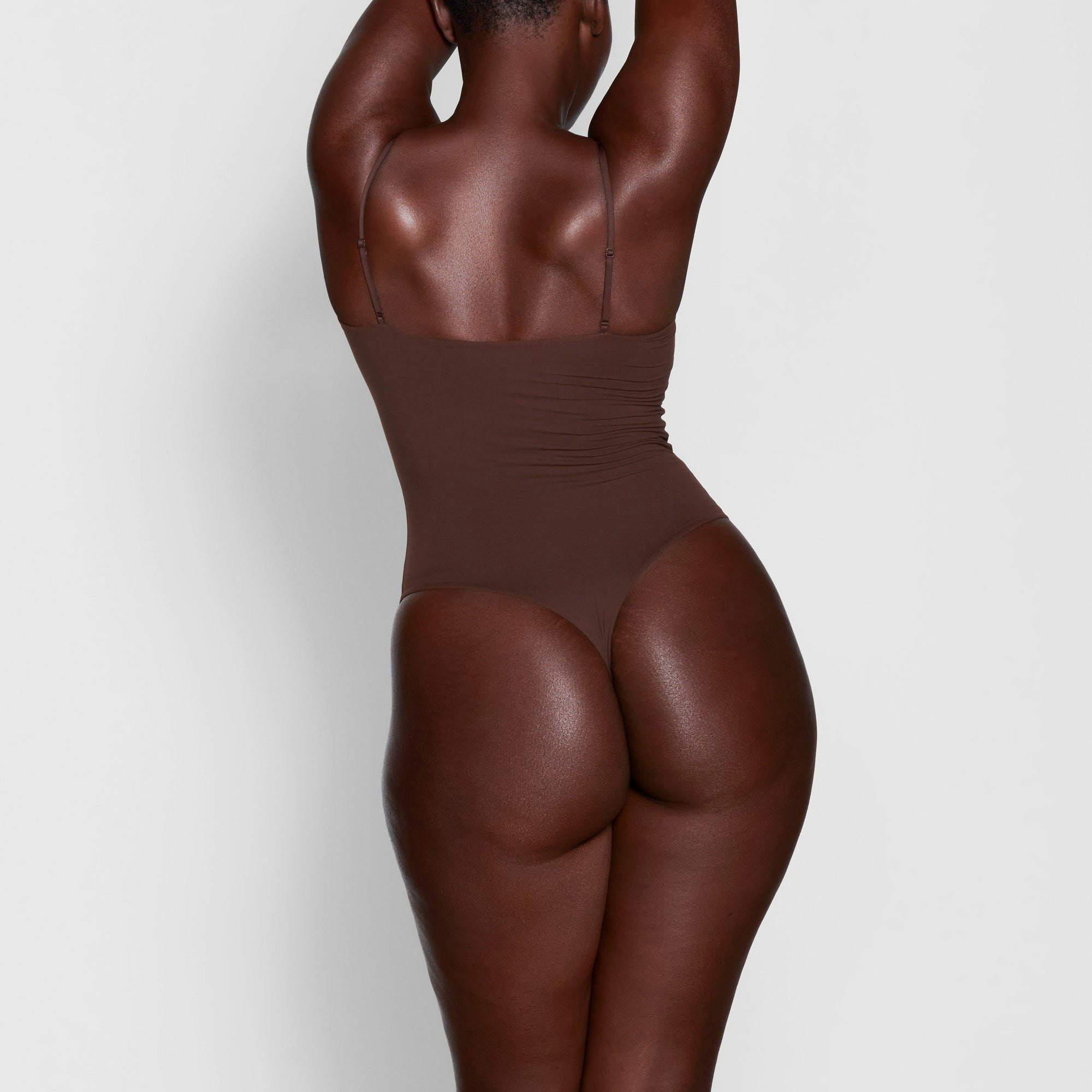 A MODEL STANDS WITH HER BACK TO THE CAMERA SHOWING THE FITS EVERYBODY CAMI BODYSUIT | COCOA