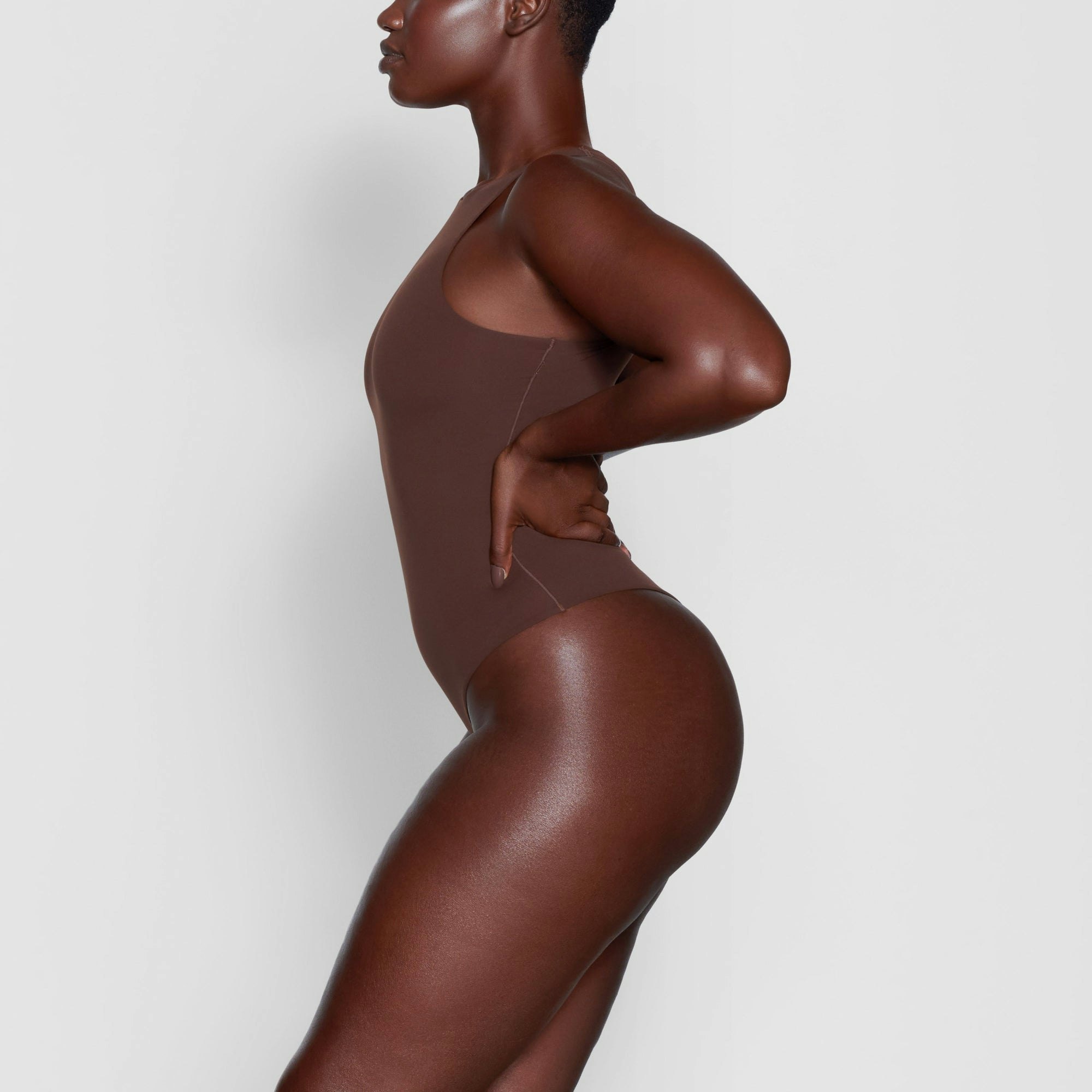 A MODEL STANDS SIDEWAYS SHOWING THE PROFILE OF THE FITS EVERYBODY HIGH NECK BODYSUIT | COCOA