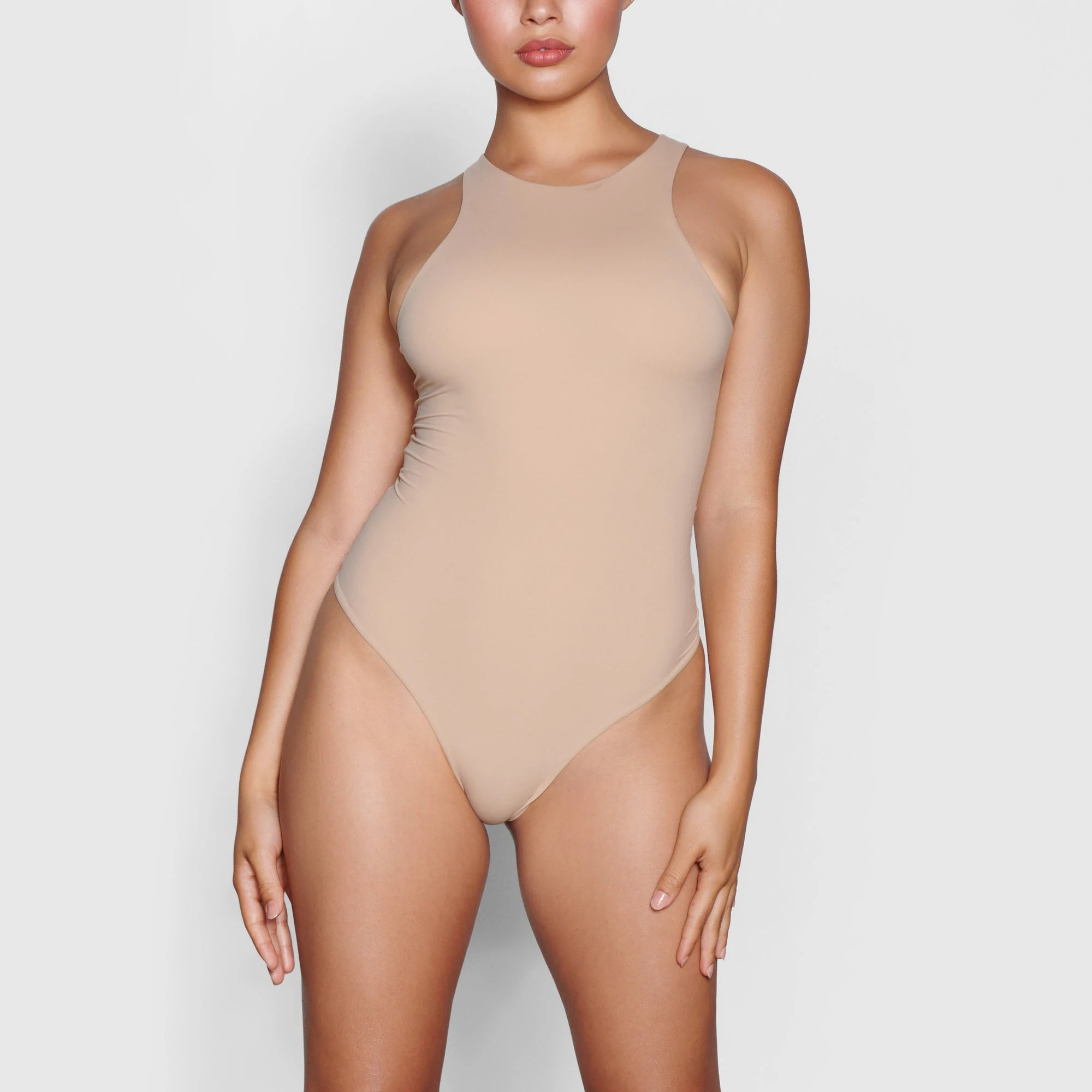 A MODEL STANDS FACING FORWARD WEARING THE SKIMS FITS EVERYBODY HIGH NECK BODYSUIT IN CLAY | SEE: S