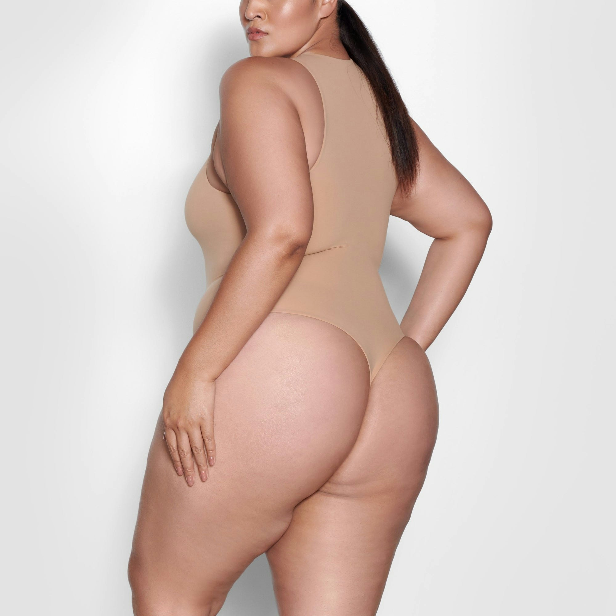 A MODEL STANDS SIDEWAYS SHOWING THE PROFILE OF THE FITS EVERYBODY HIGH NECK BODYSUIT | OCHRE