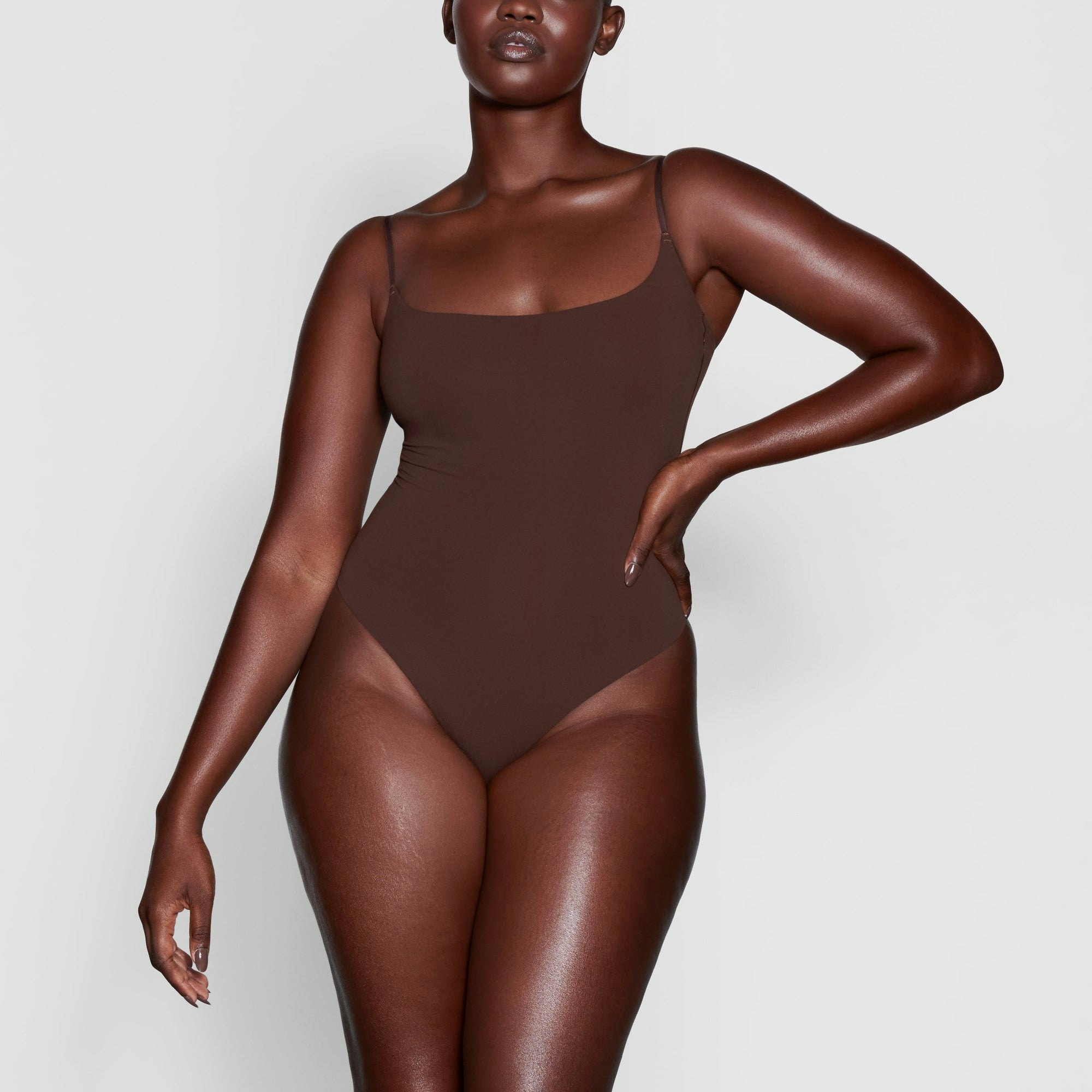 A MODEL STANDS FACING FORWARD WEARING THE SKIMS FITS EVERYBODY CAMI BODYSUIT IN COCOA | SEE: L