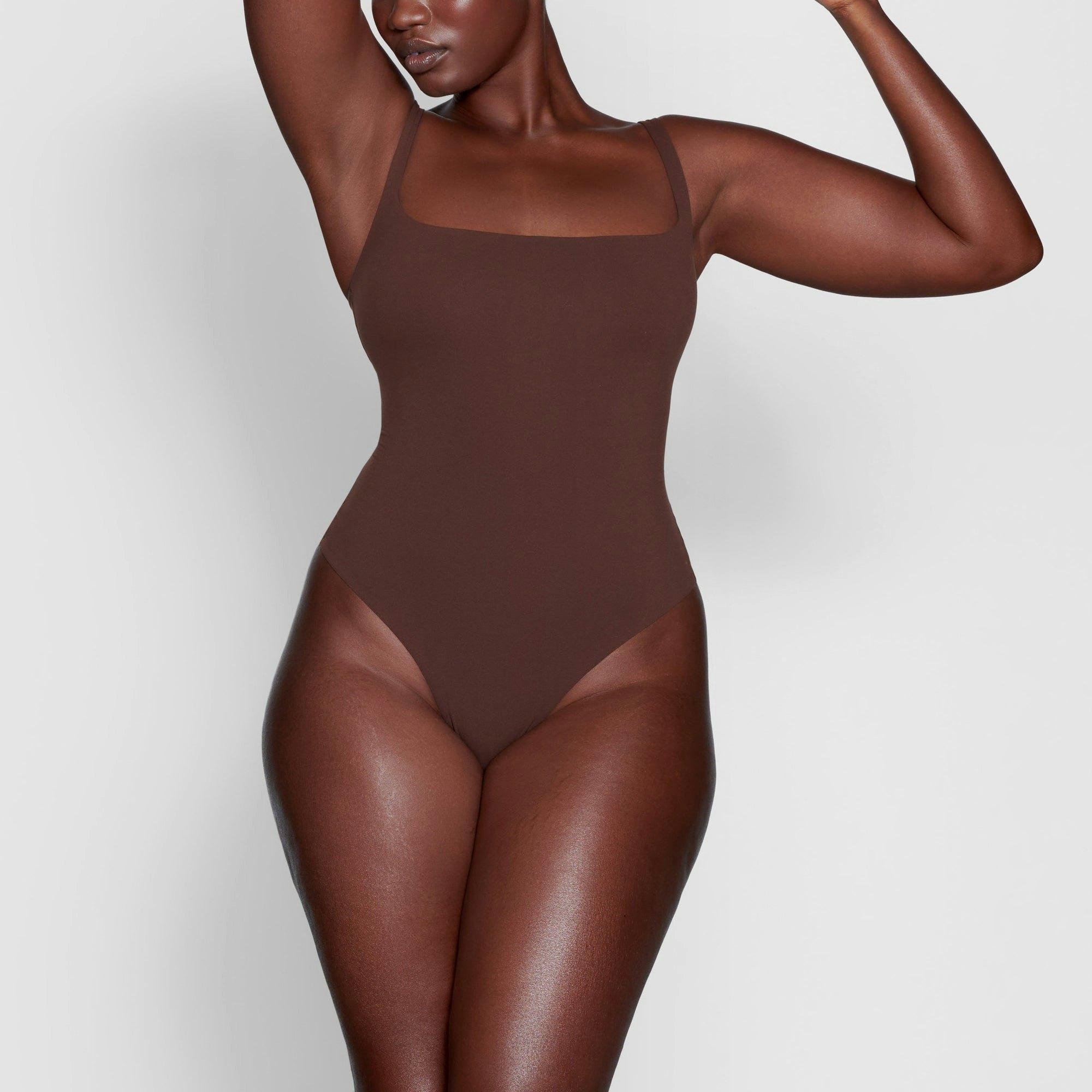 A MODEL STANDS FACING FORWARD WEARING THE SKIMS FITS EVERYBODY SQUARE NECK BODYSUIT IN COCOA | SEE: L
