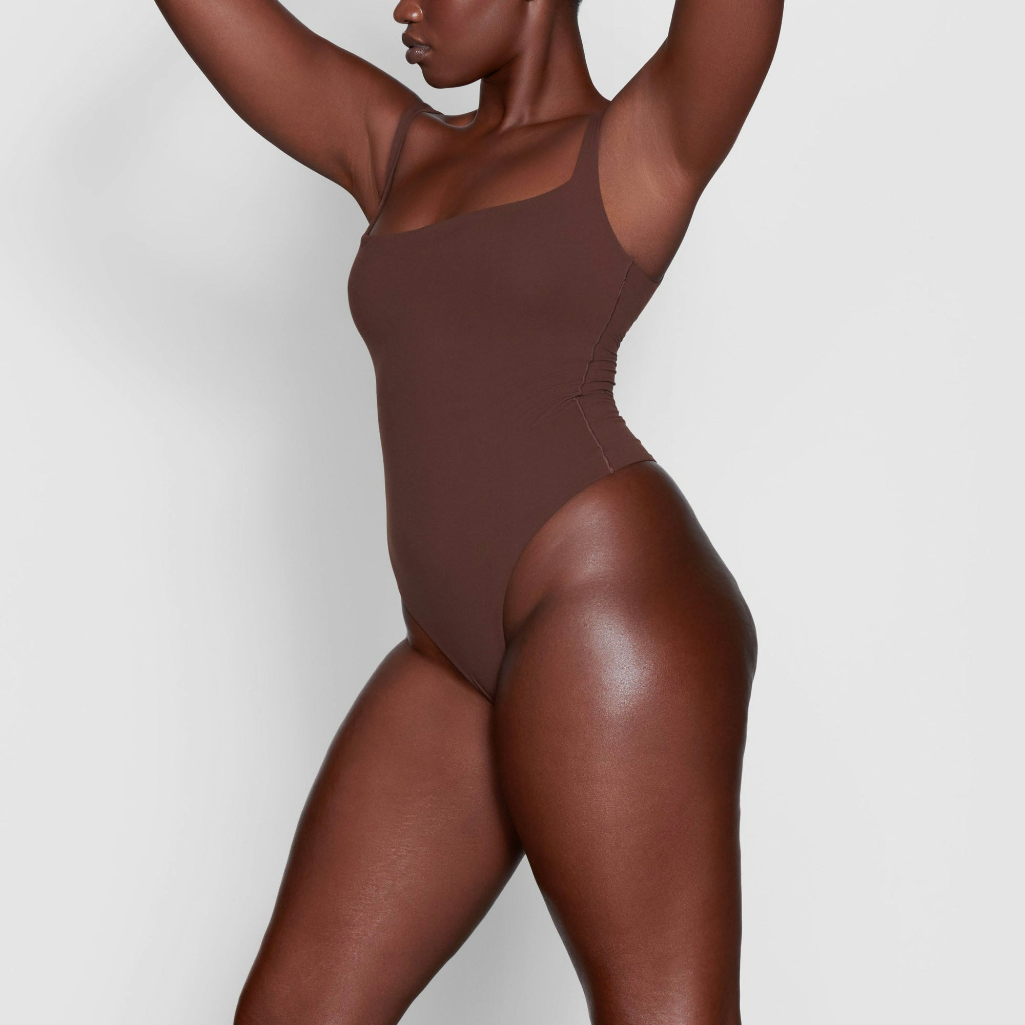 A MODEL STANDS SIDEWAYS SHOWING THE PROFILE OF THE FITS EVERYBODY SQUARE NECK BODYSUIT | COCOA