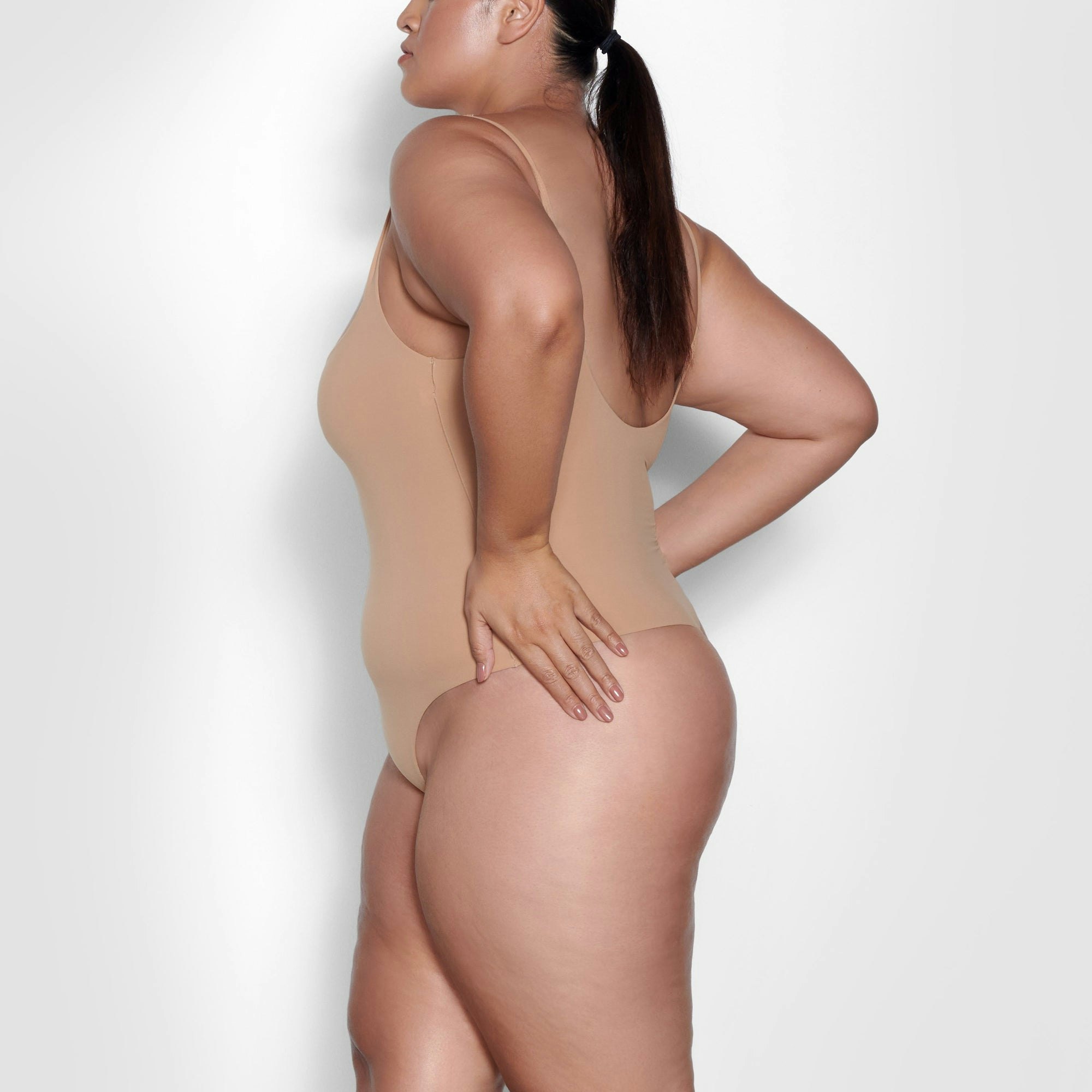 A MODEL STANDS SIDEWAYS SHOWING THE PROFILE OF THE FITS EVERYBODY SQUARE NECK BODYSUIT | OCHRE