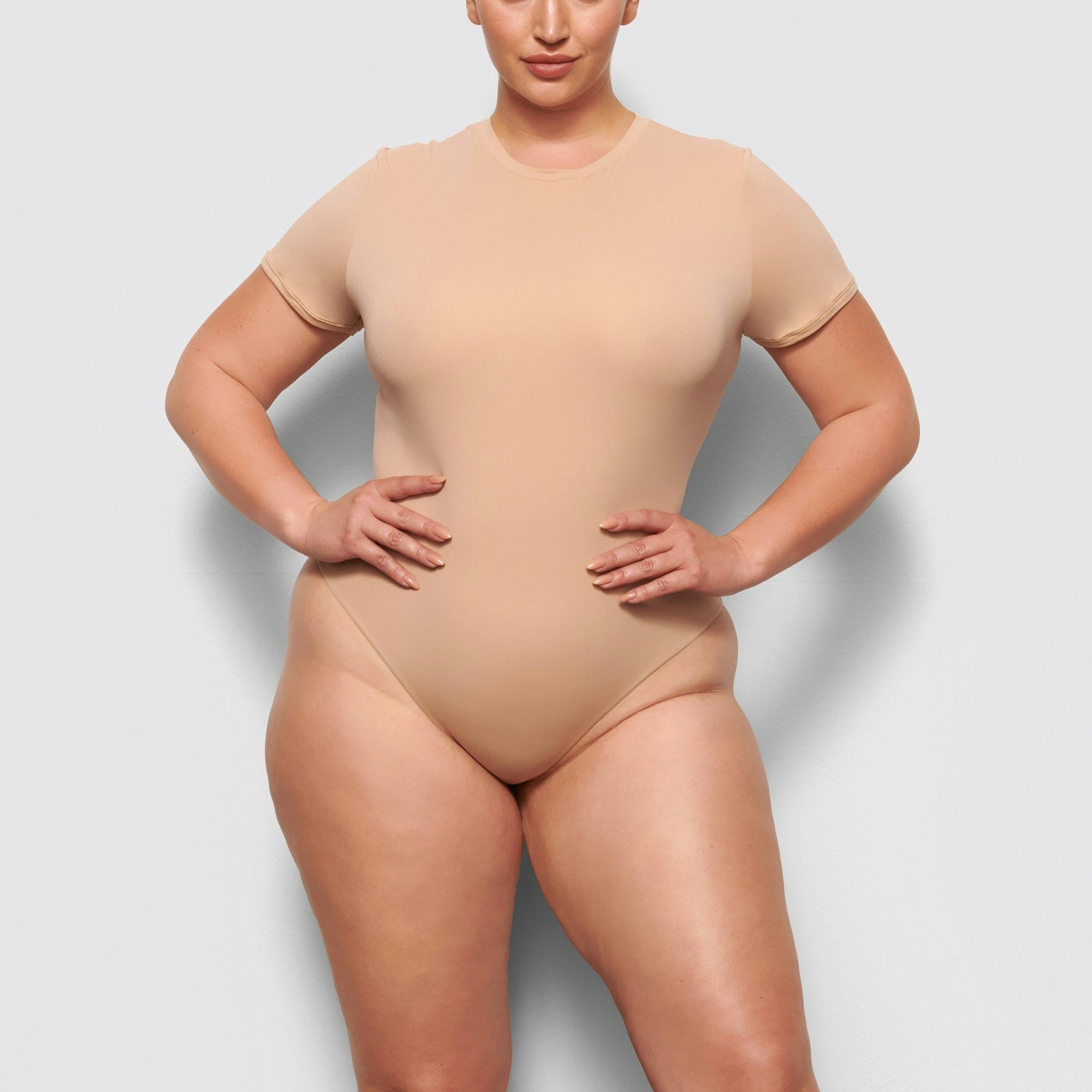 A MODEL STANDS FACING FORWARD WEARING THE SKIMS FITS EVERYBODY T-SHIRT BODYSUIT IN MICA | SEE: 2X, 3X, 4X