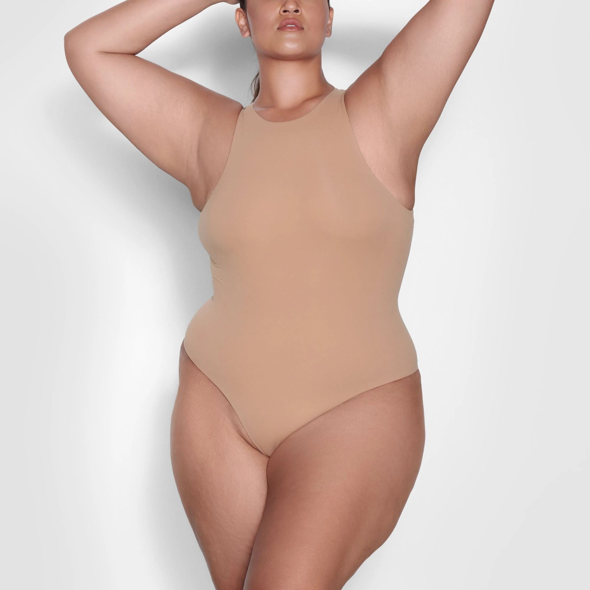 A MODEL STANDS FACING FORWARD WEARING THE SKIMS FITS EVERYBODY HIGH NECK BODYSUIT IN OCHRE | SEE: 3X