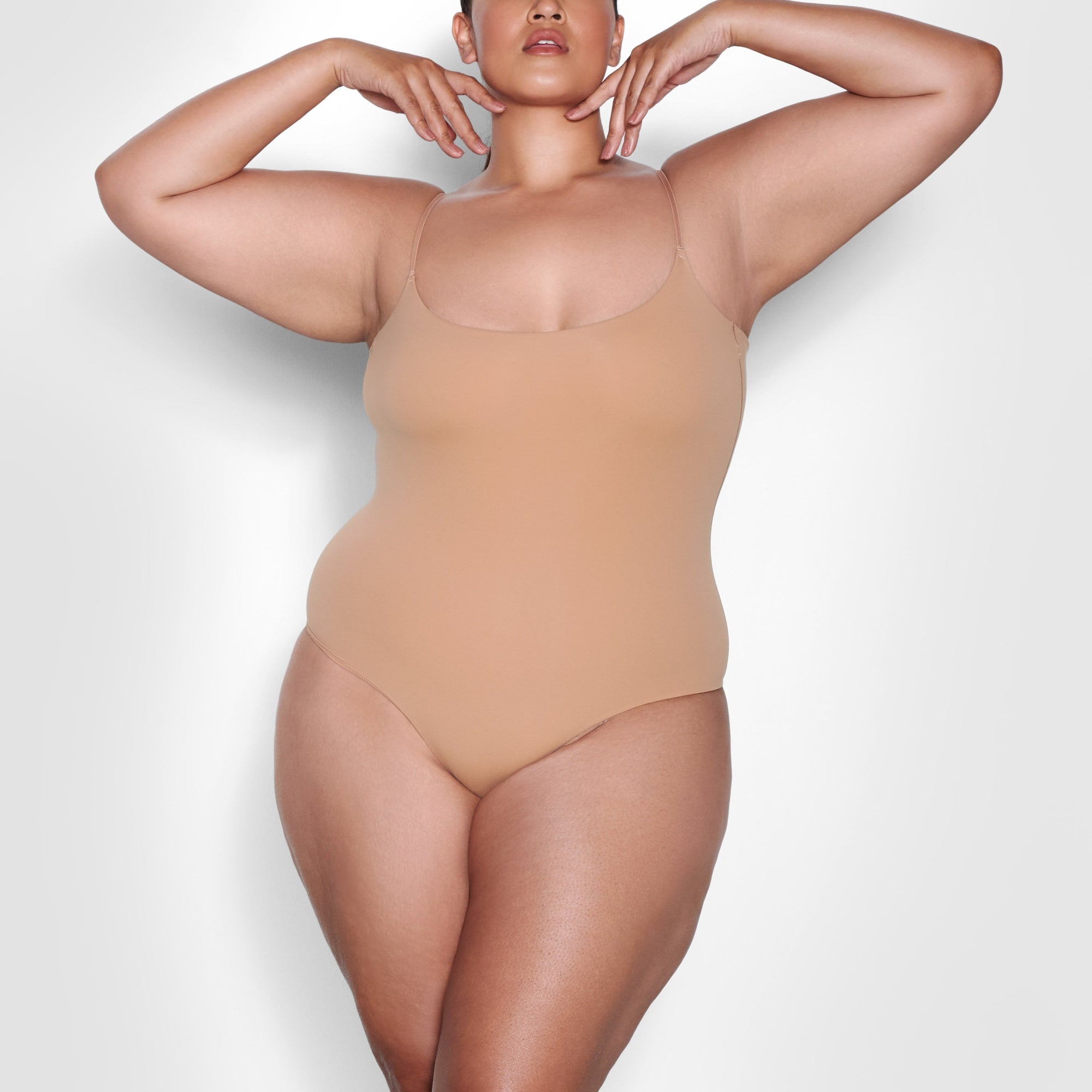 A MODEL STANDS FACING FORWARD WEARING THE SKIMS FITS EVERYBODY CAMI BODYSUIT IN OCHRE | SEE: 2X, 3X, 4X