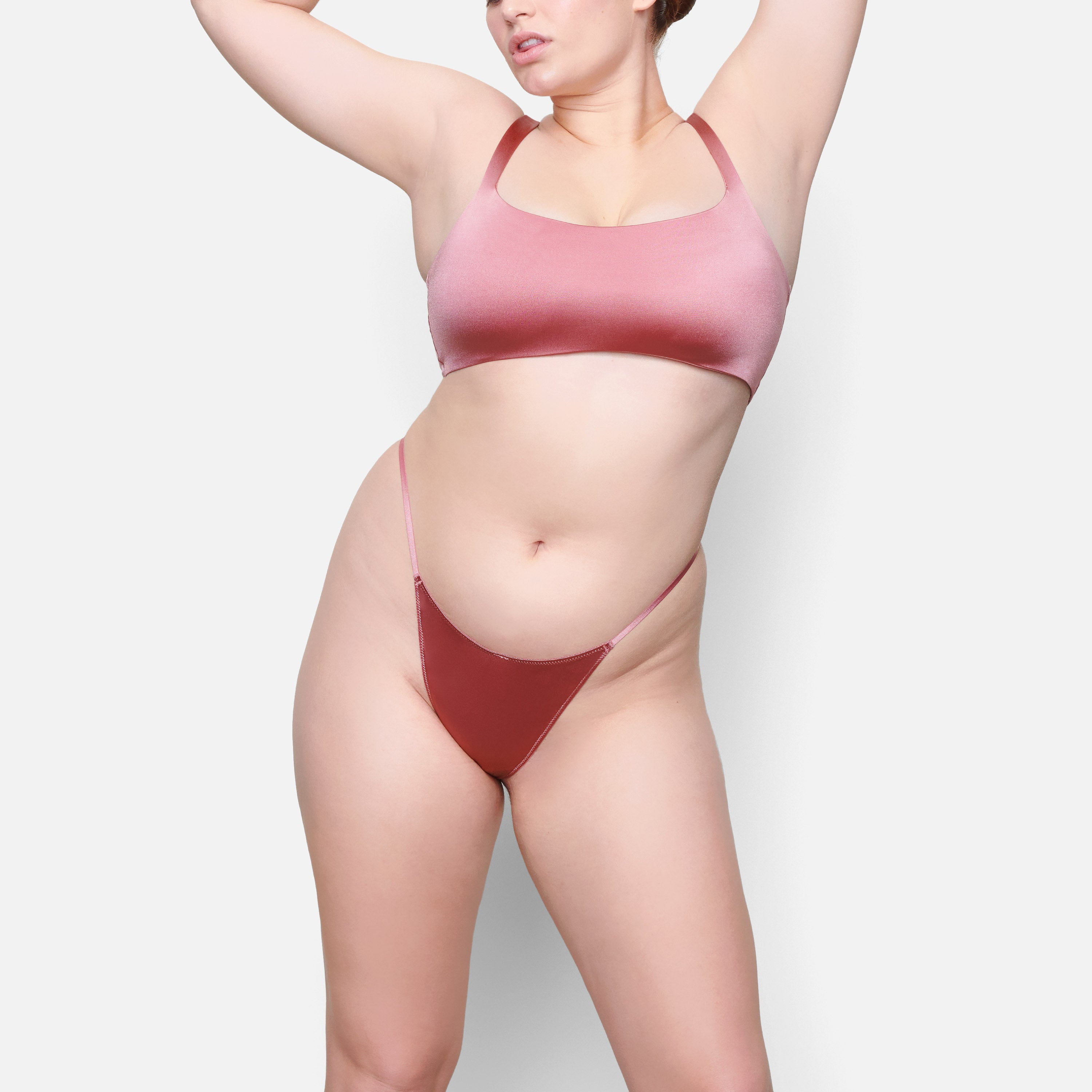 A MODEL STANDS FACING FORWARD WEARING THE SKIMS STRETCH SATIN SQUARE NECK BRA IN DAHLIA | SEE: M, L, XL