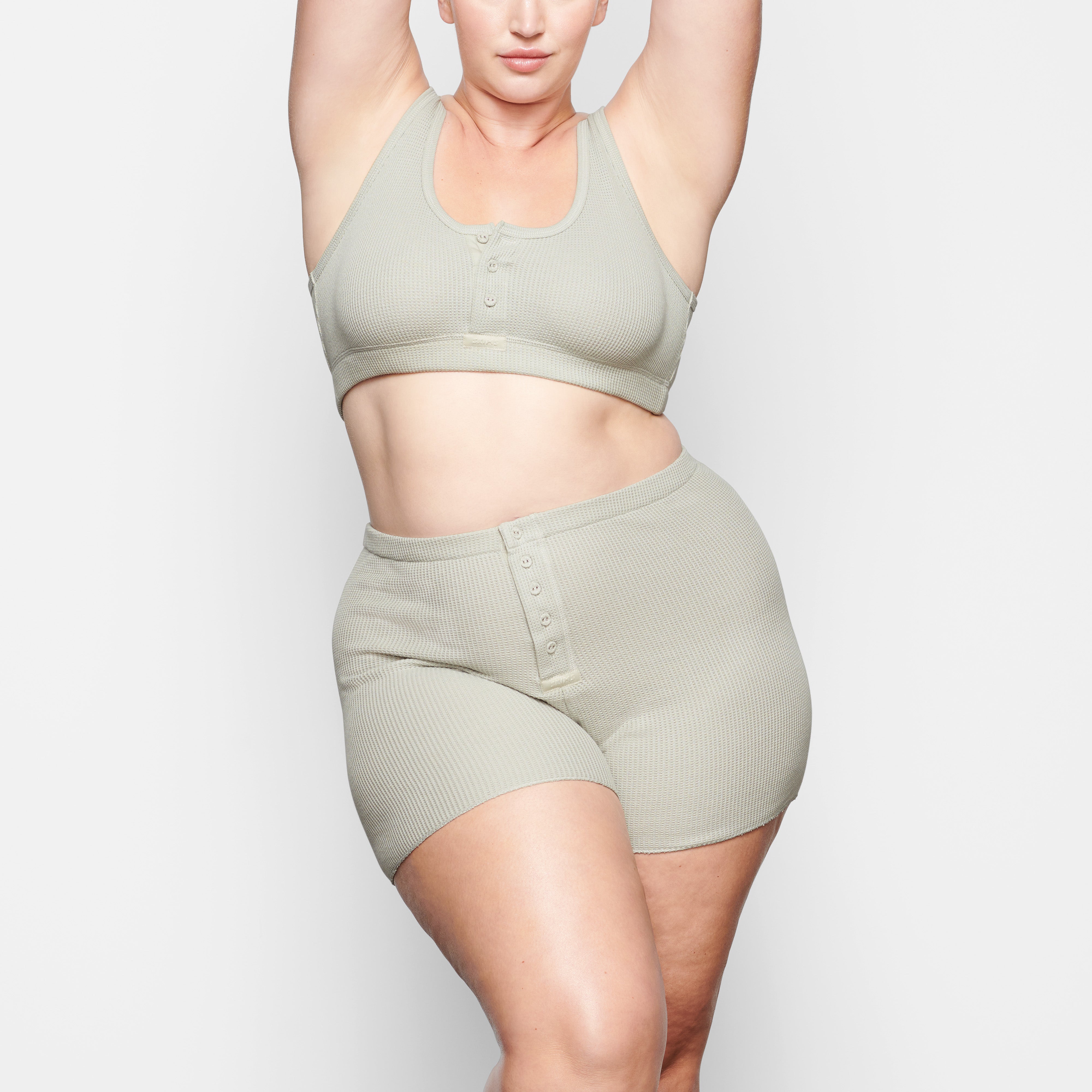 A MODEL STANDS FACING FORWARD WEARING THE SKIMS WAFFLE HENLEY BRA IN TALC | SEE: 2X, 3X, 4X