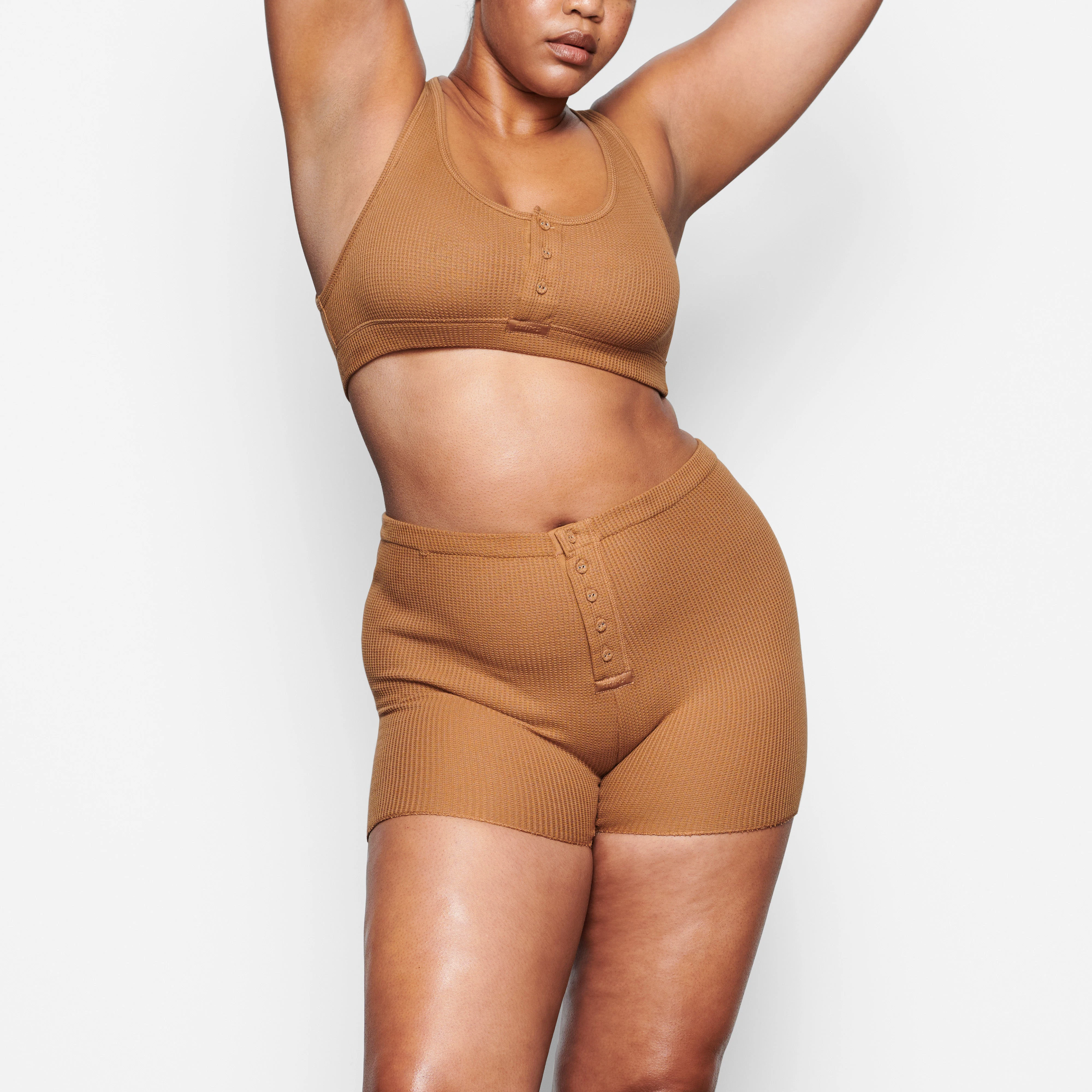 A MODEL STANDS FACING FORWARD WEARING THE SKIMS WAFFLE HENLEY BRA IN CAMEL | SEE: M, L, XL