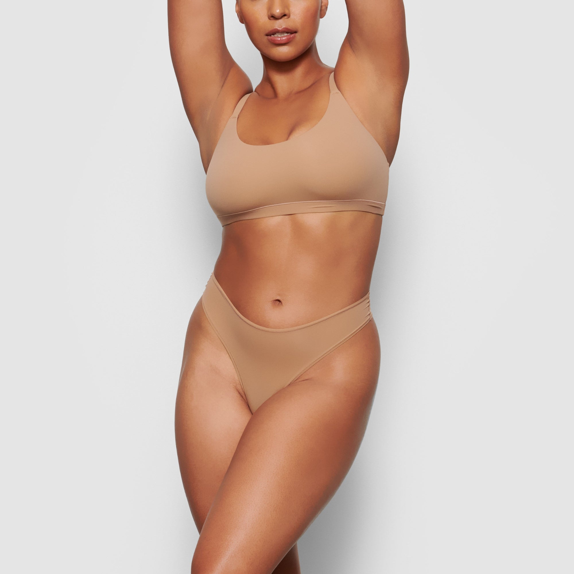 A MODEL STANDS FACING FORWARD WEARING THE SKIMS FITS EVERYBODY SCOOP NECK BRA IN SIENNA | SEE: M, L, XL