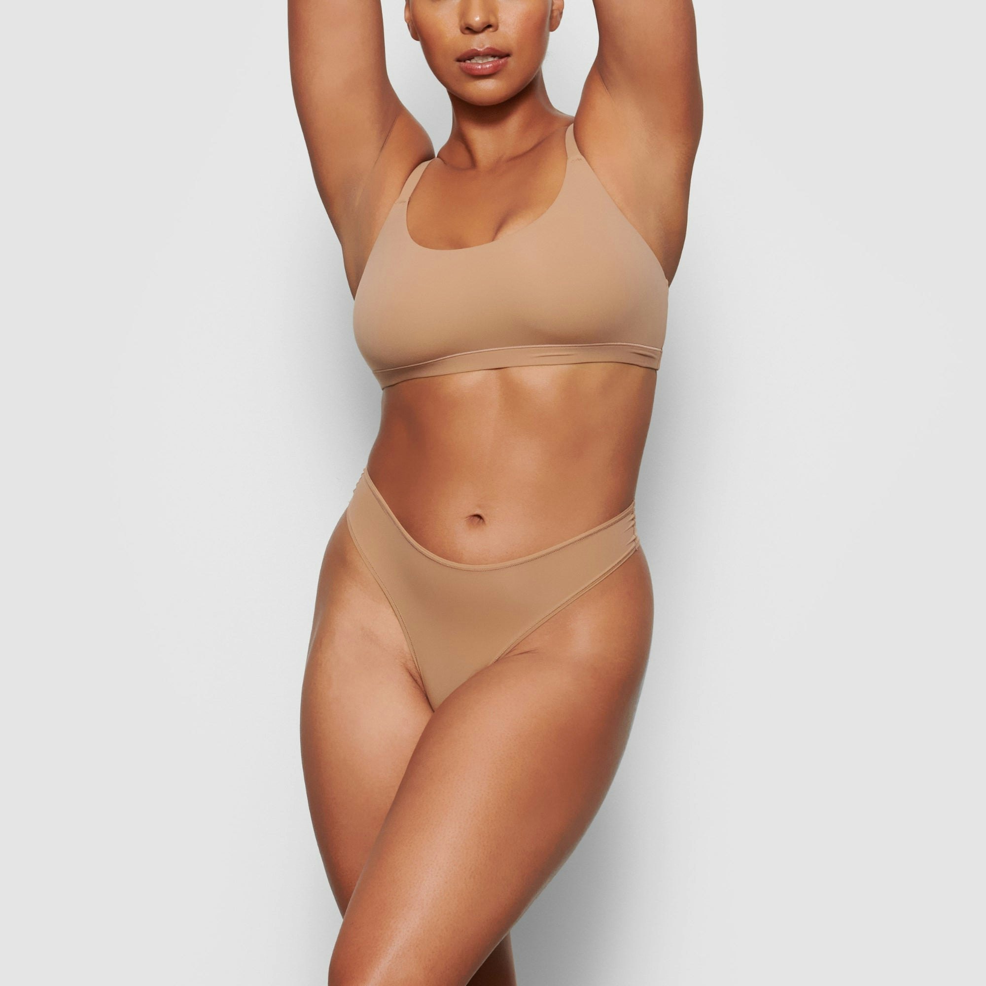 A MODEL STANDS FACING FORWARD WEARING THE SKIMS FITS EVERYBODY SCOOP NECK BRA IN SIENNA | SEE: M, L, XL
