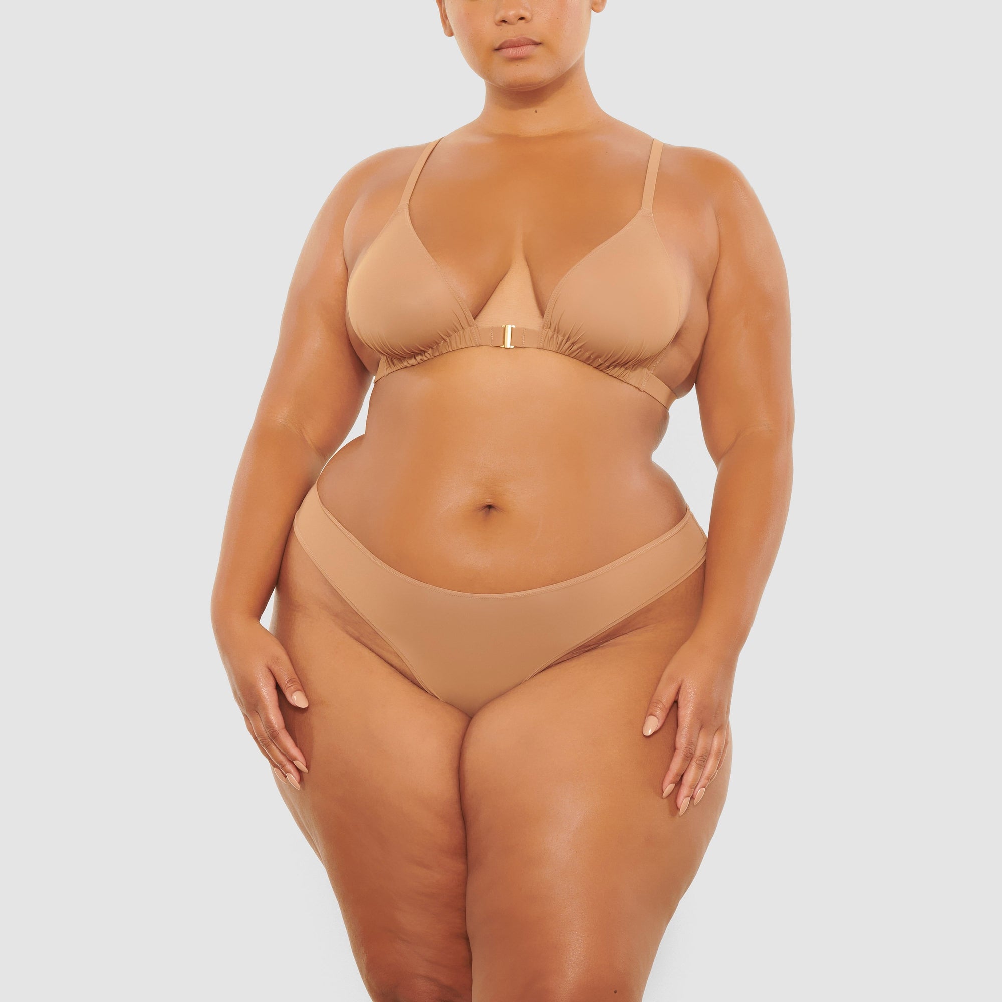 A MODEL STANDS FACING FORWARD WEARING THE SKIMS JELLY SHEER TRIANGLE BRALETTE IN SIENNA | SEE: 2X, 3X, 4X