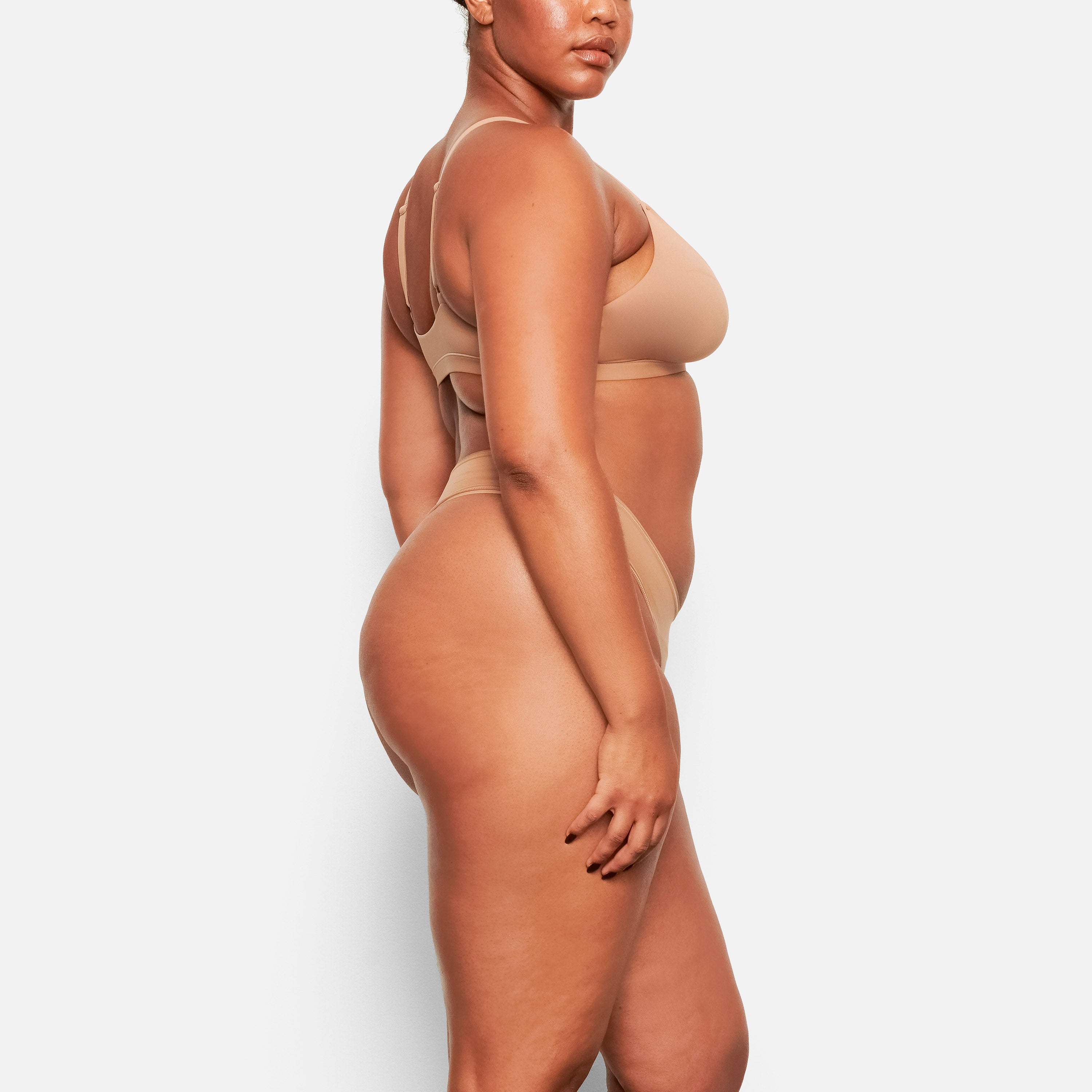 A MODEL STANDS FACING FORWARD WEARING THE SKIMS FITS EVERYBODY TRIANGLE BRALETTE IN SIENNA | 