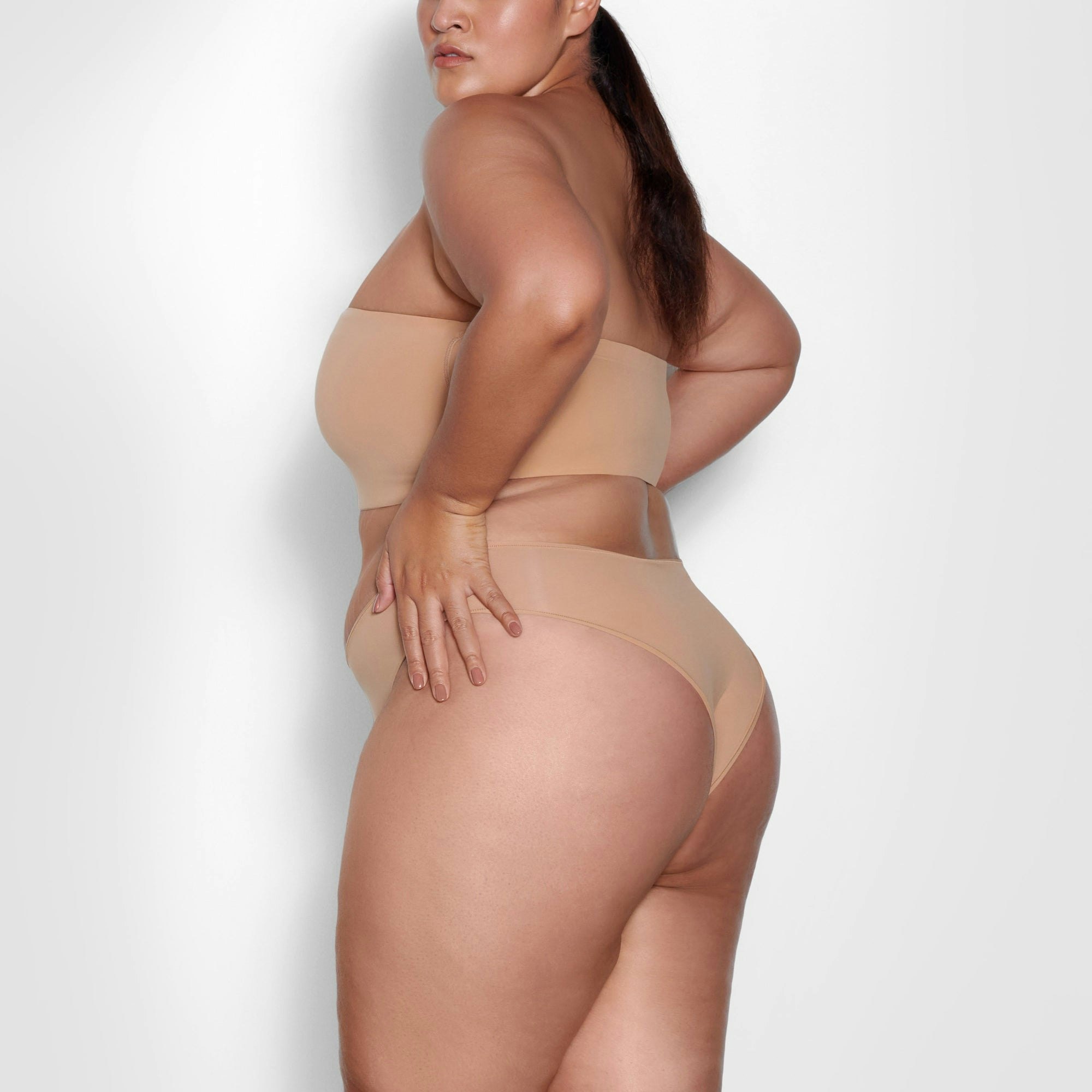 A MODEL STANDS SIDEWAYS SHOWING THE PROFILE OF THE FITS EVERYBODY BANDEAU BRA | OCHRE