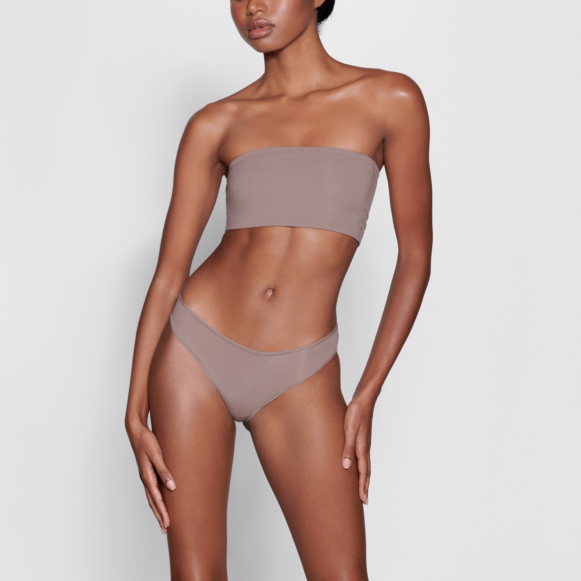 A MODEL STANDS FACING FORWARD WEARING THE SKIMS FITS EVERYBODY BANDEAU BRA IN UMBER | SEE: XXS, XS