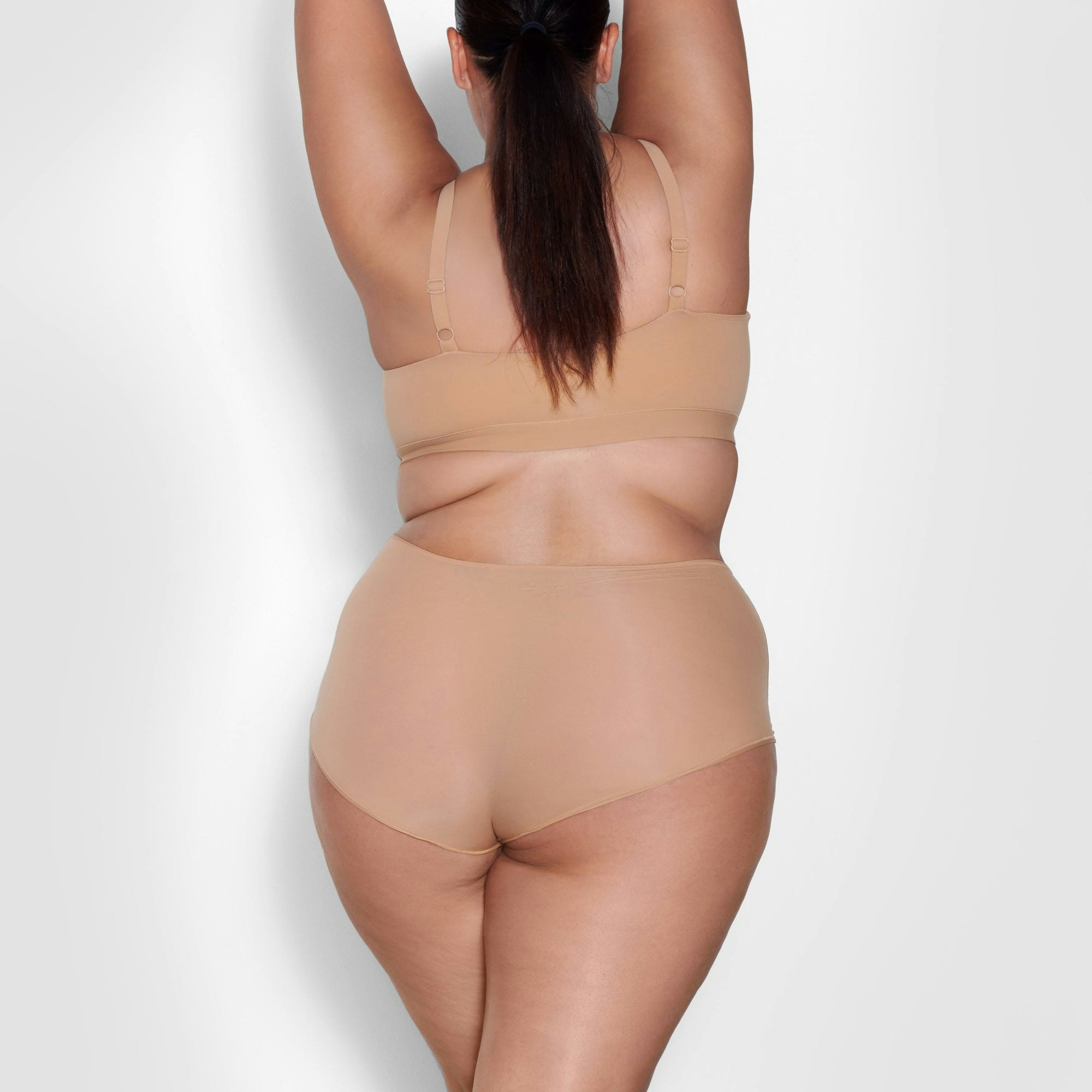 A MODEL STANDS WITH HER BACK TO THE CAMERA SHOWING THE FITS EVERYBODY SCOOP NECK BRA | OCHRE