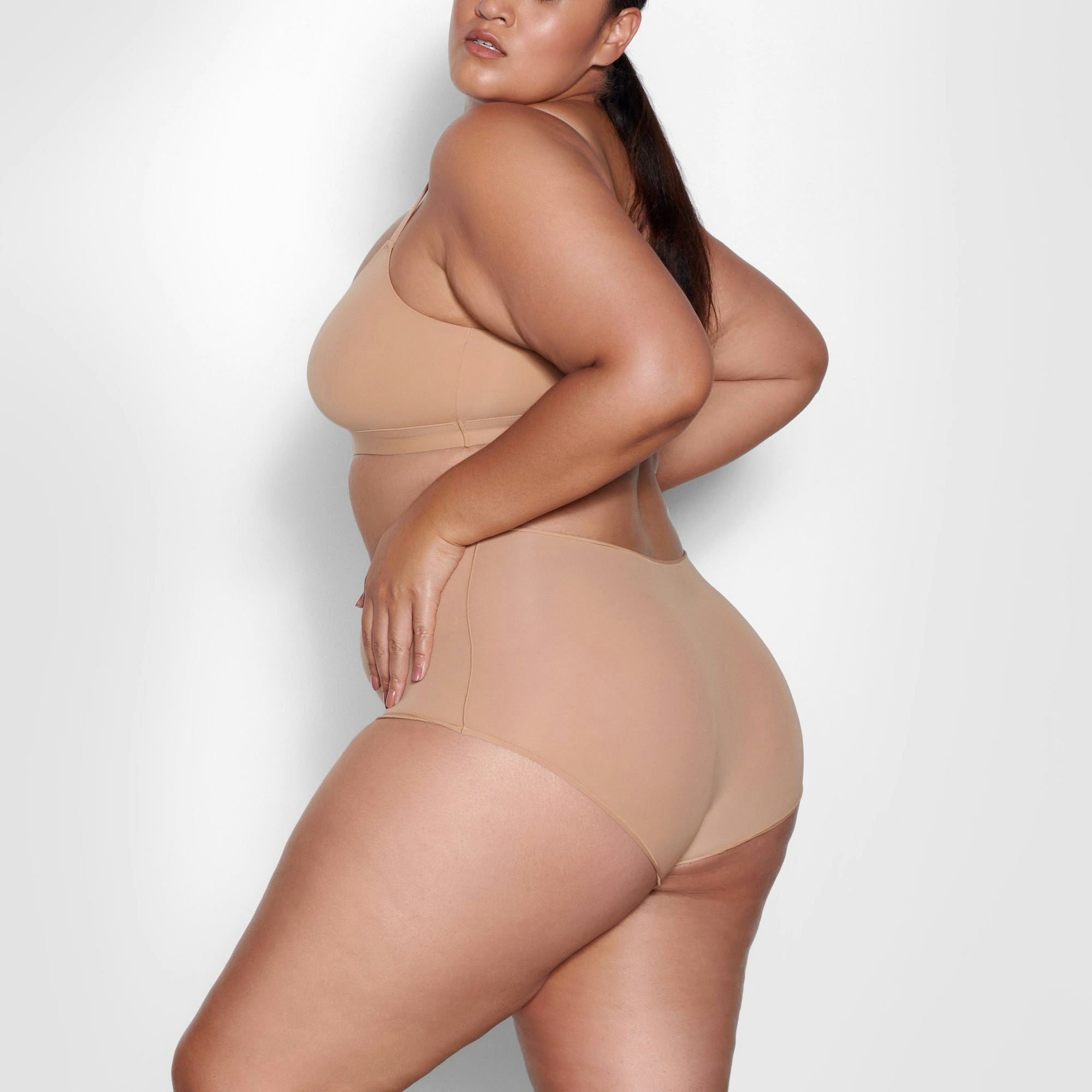 A MODEL STANDS SIDEWAYS SHOWING THE PROFILE OF THE FITS EVERYBODY SCOOP NECK BRA | OCHRE