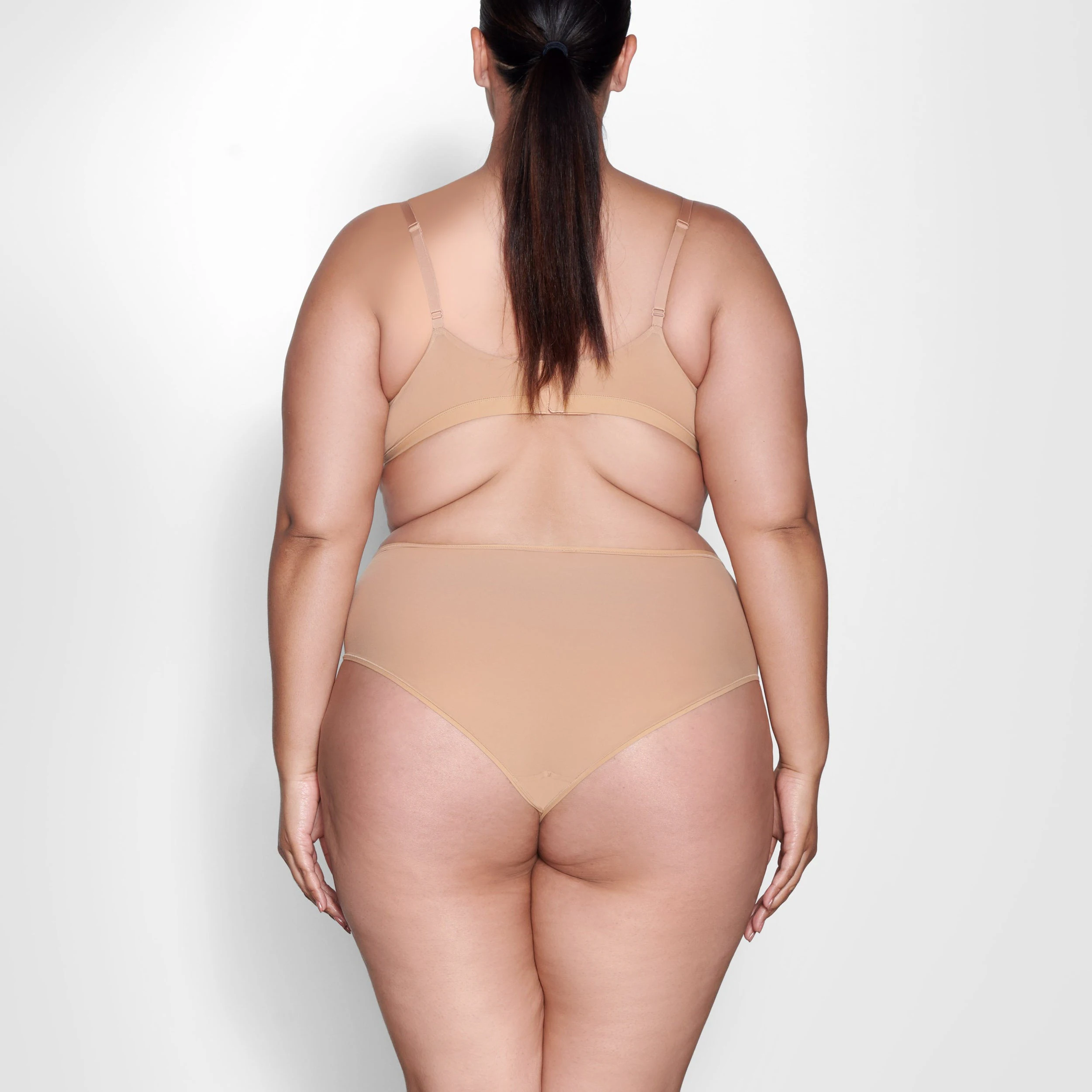 A MODEL STANDS WITH HER BACK TO THE CAMERA SHOWING THE FITS EVERYBODY CROSSOVER BRALETTE | OCHRE