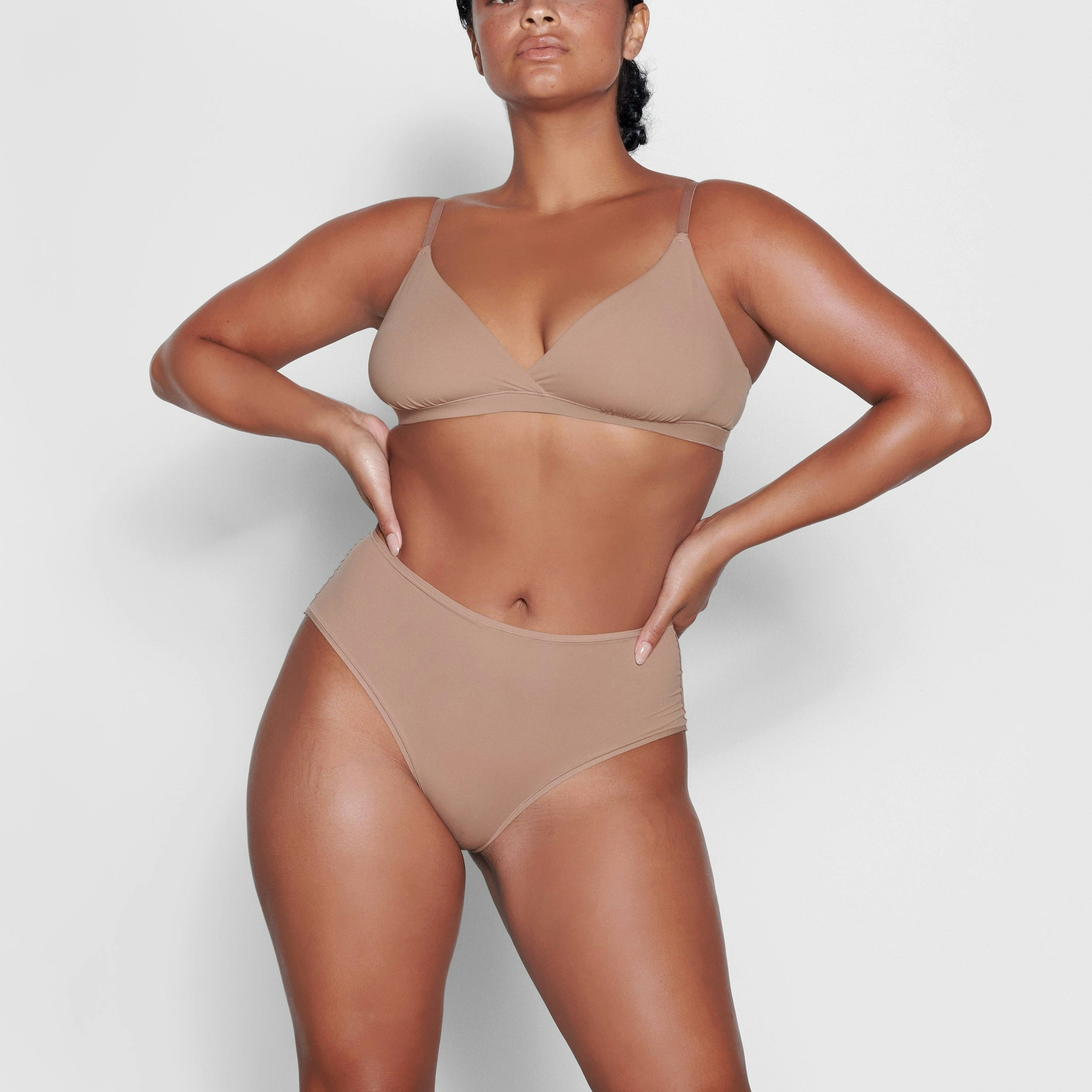 A MODEL STANDS FACING FORWARD WEARING THE SKIMS FITS EVERYBODY CROSSOVER BRALETTE IN SIENNA | SEE: M, L