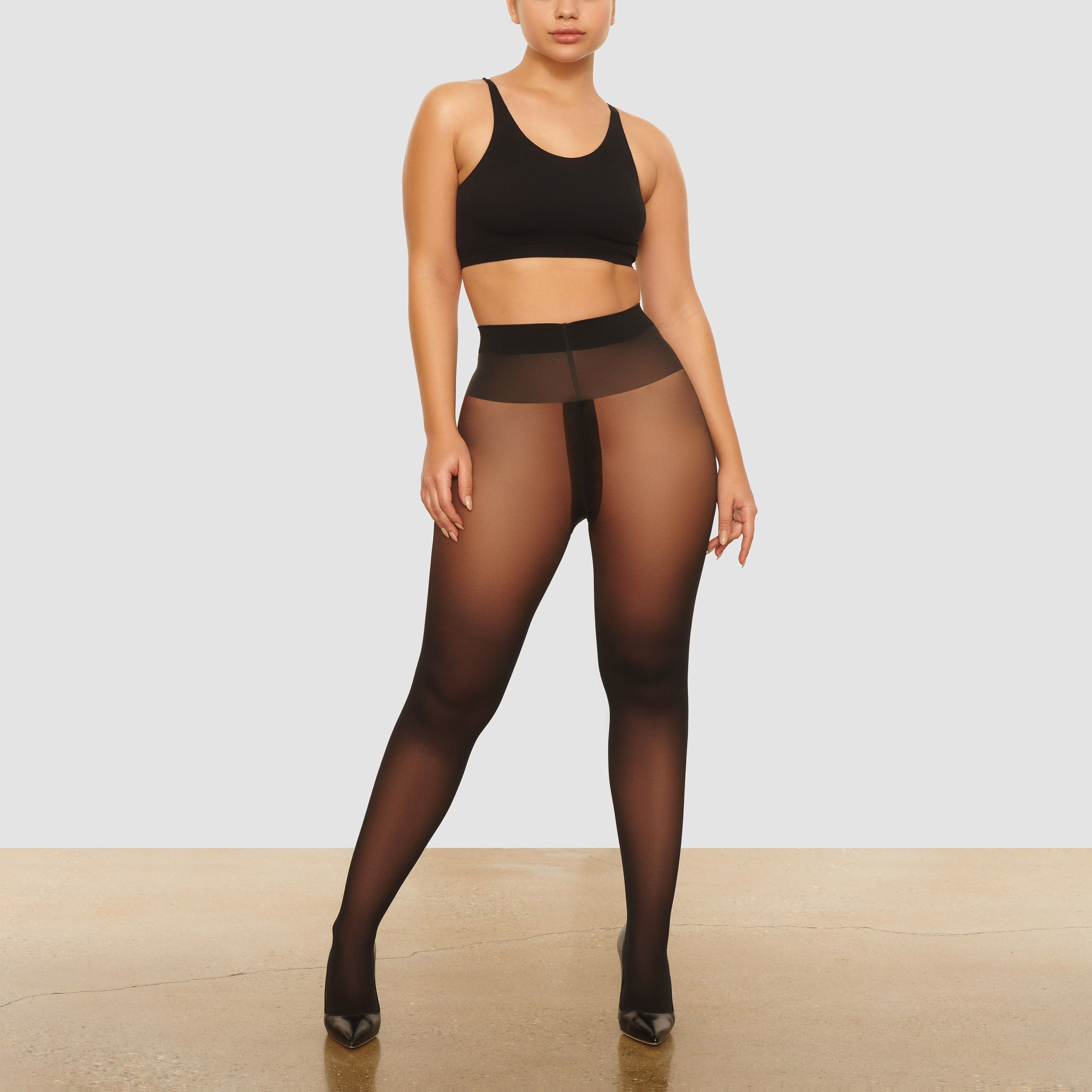 A MODEL STANDS FACING FORWARD WEARING THE SKIMS NUDE SUPPORT TIGHTS IN ONYX | SEE: XXS, XS