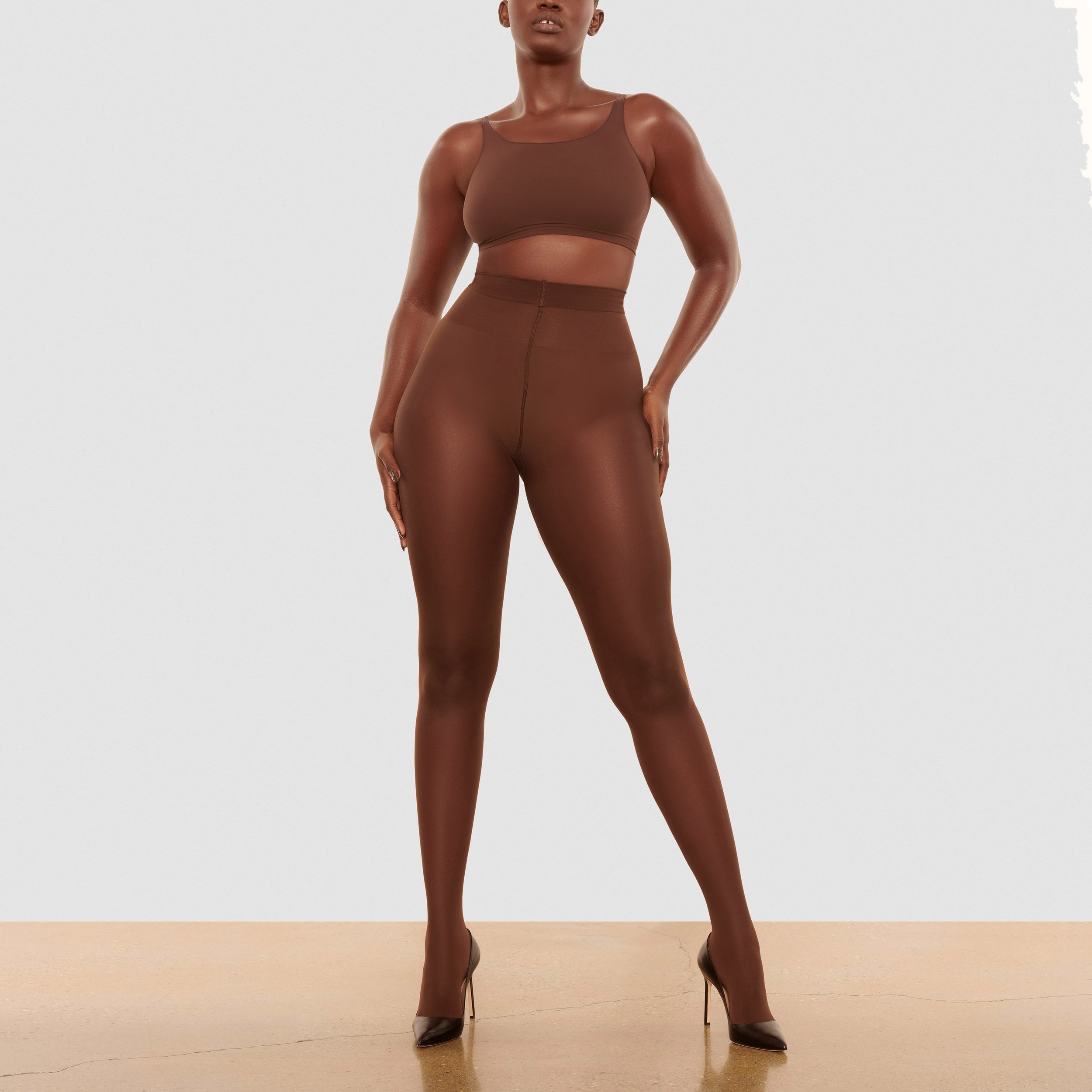 A MODEL STANDS FACING FORWARD WEARING THE SKIMS NUDE SUPPORT TIGHTS IN COCOA | SEE: L, XL