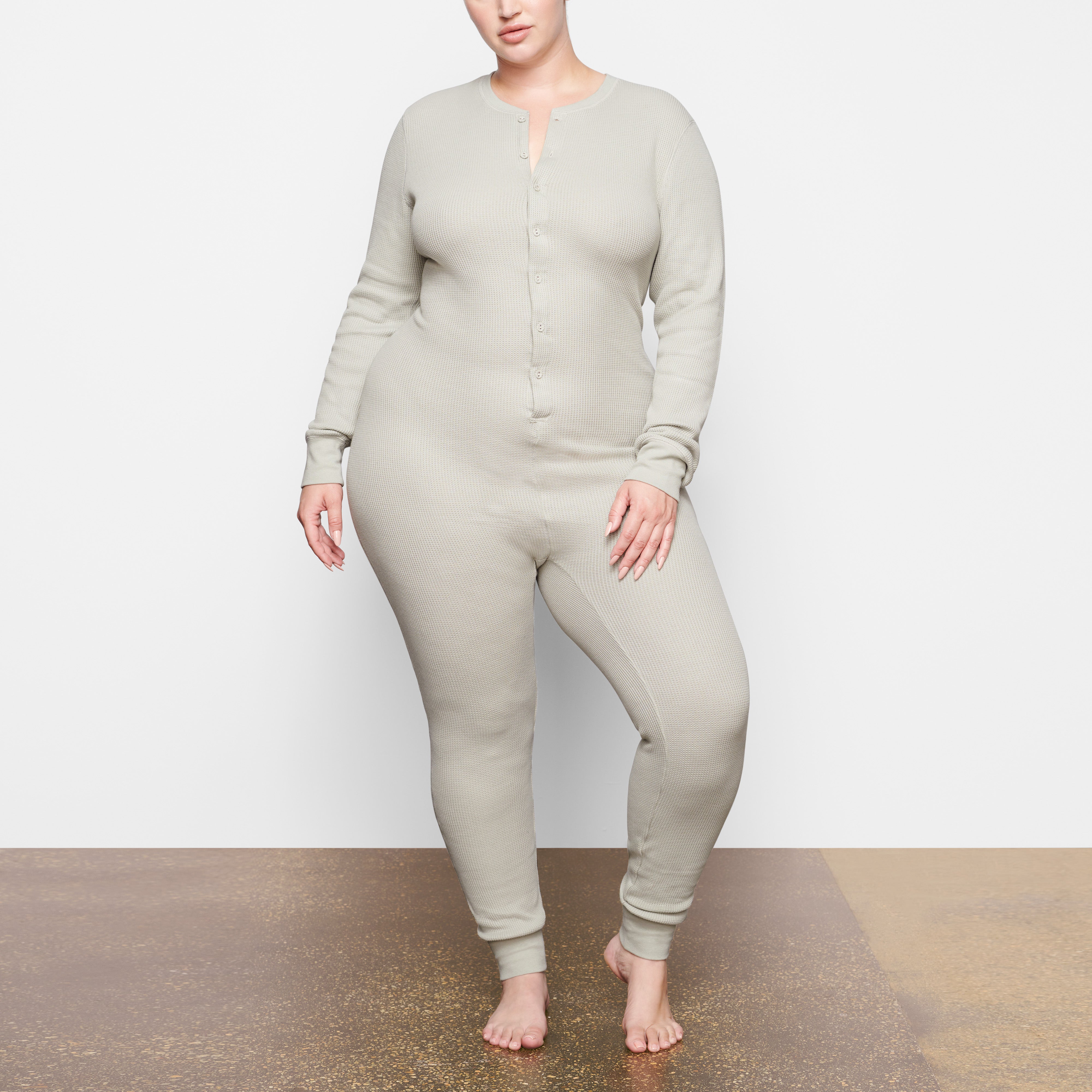 A MODEL STANDS FACING FORWARD WEARING THE SKIMS WAFFLE ONESIE IN TALC | SEE: 2X, 3X, 4X