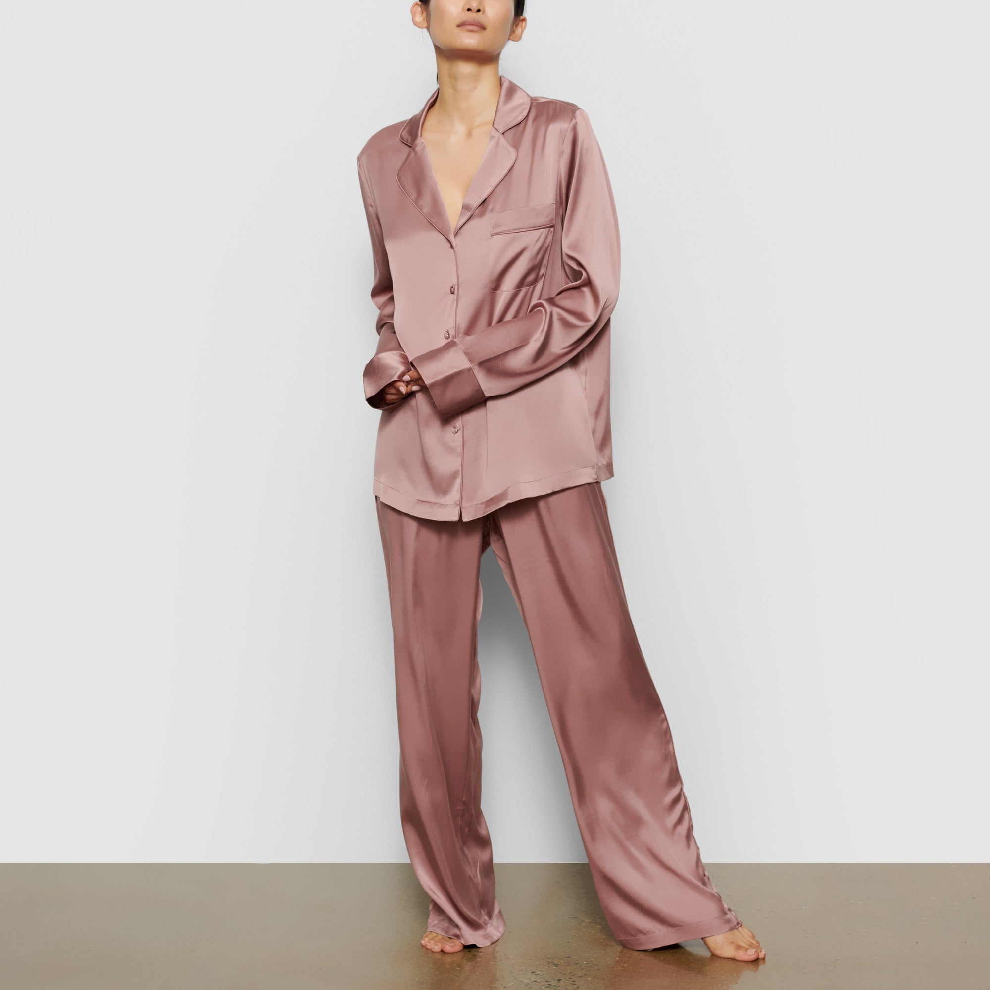 A MODEL STANDS FACING FORWARD WEARING THE SKIMS SILK SLEEP PANT IN ROSE | SEE: XXS, XS, S
