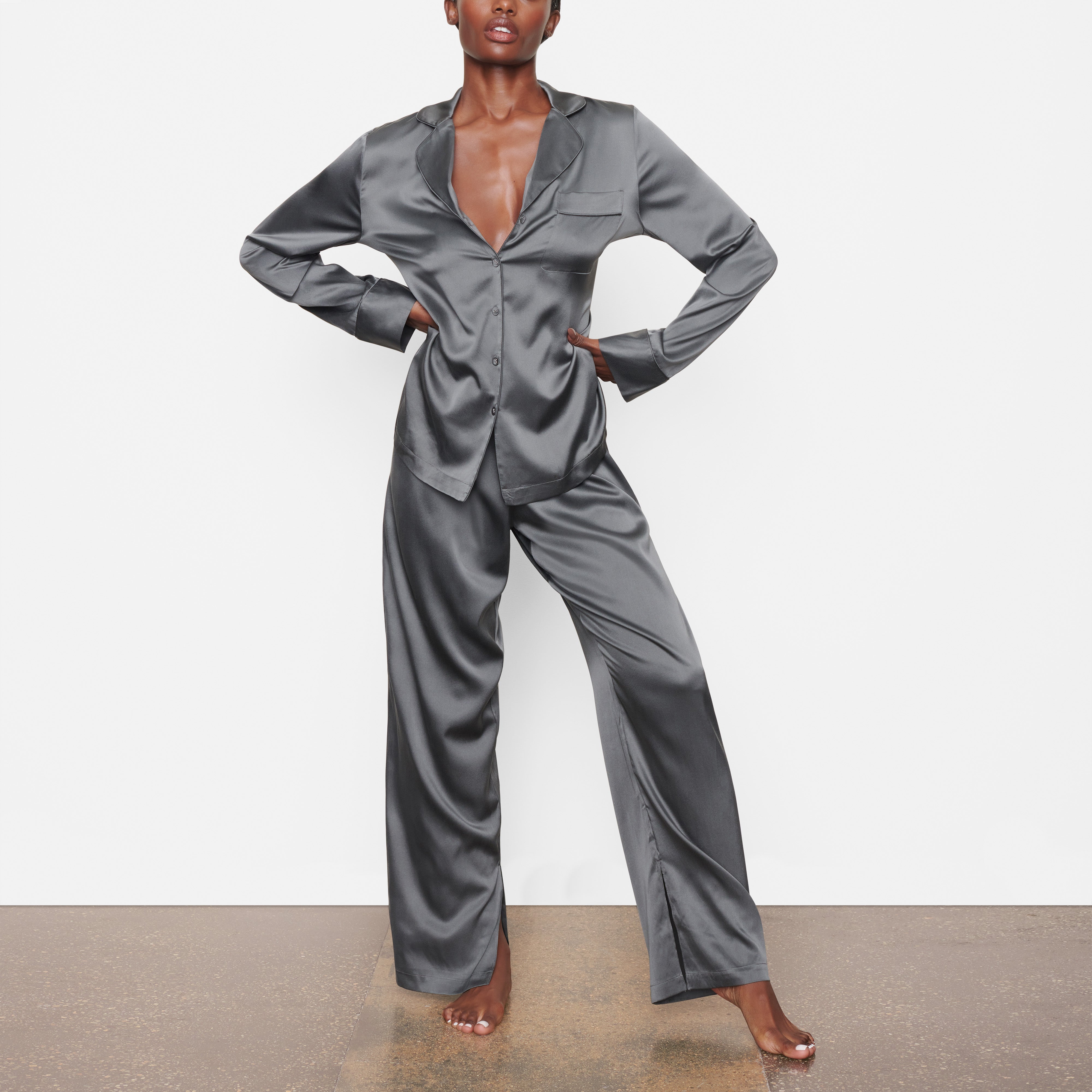 A MODEL STANDS FACING FORWARD WEARING THE SKIMS SILK SLEEP PANT IN GUNMETAL | SEE: XXS, XS, S
