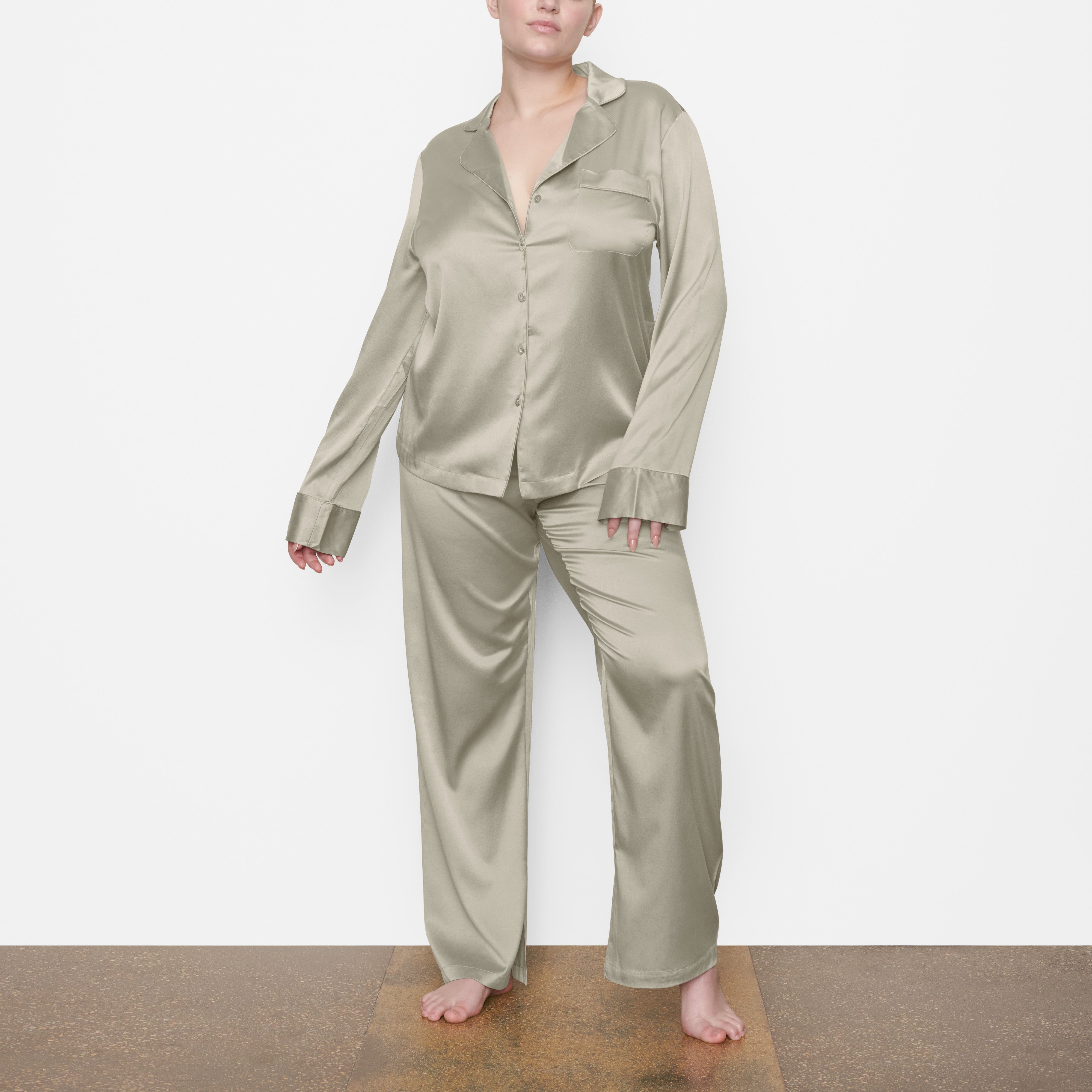 A MODEL STANDS FACING FORWARD WEARING THE SKIMS SILK SLEEP PANT IN TALC | SEE: M, L, XL