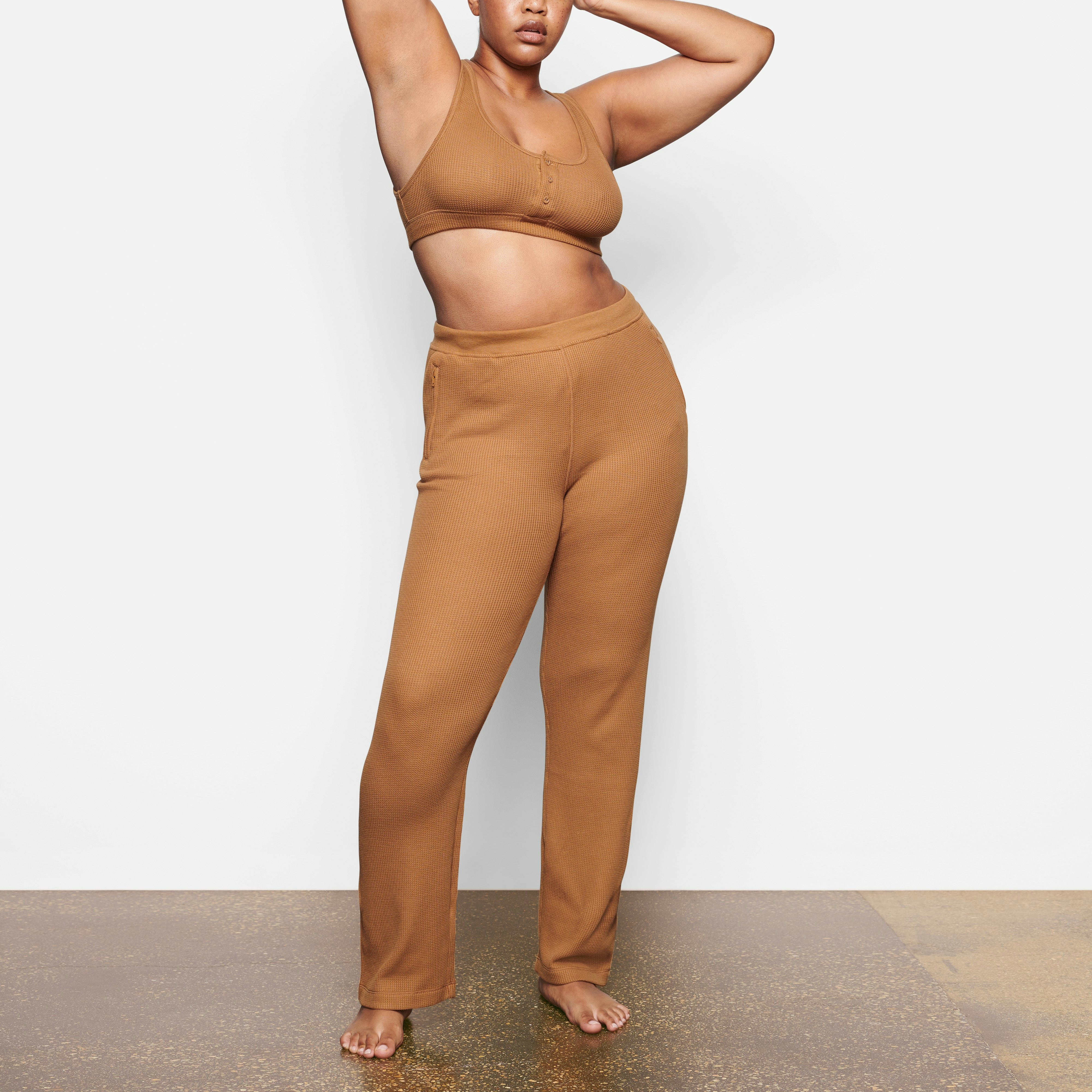 A MODEL STANDS FACING FORWARD WEARING THE SKIMS WAFFLE LOOSE PANT IN CAMEL | SEE: M, L, XL