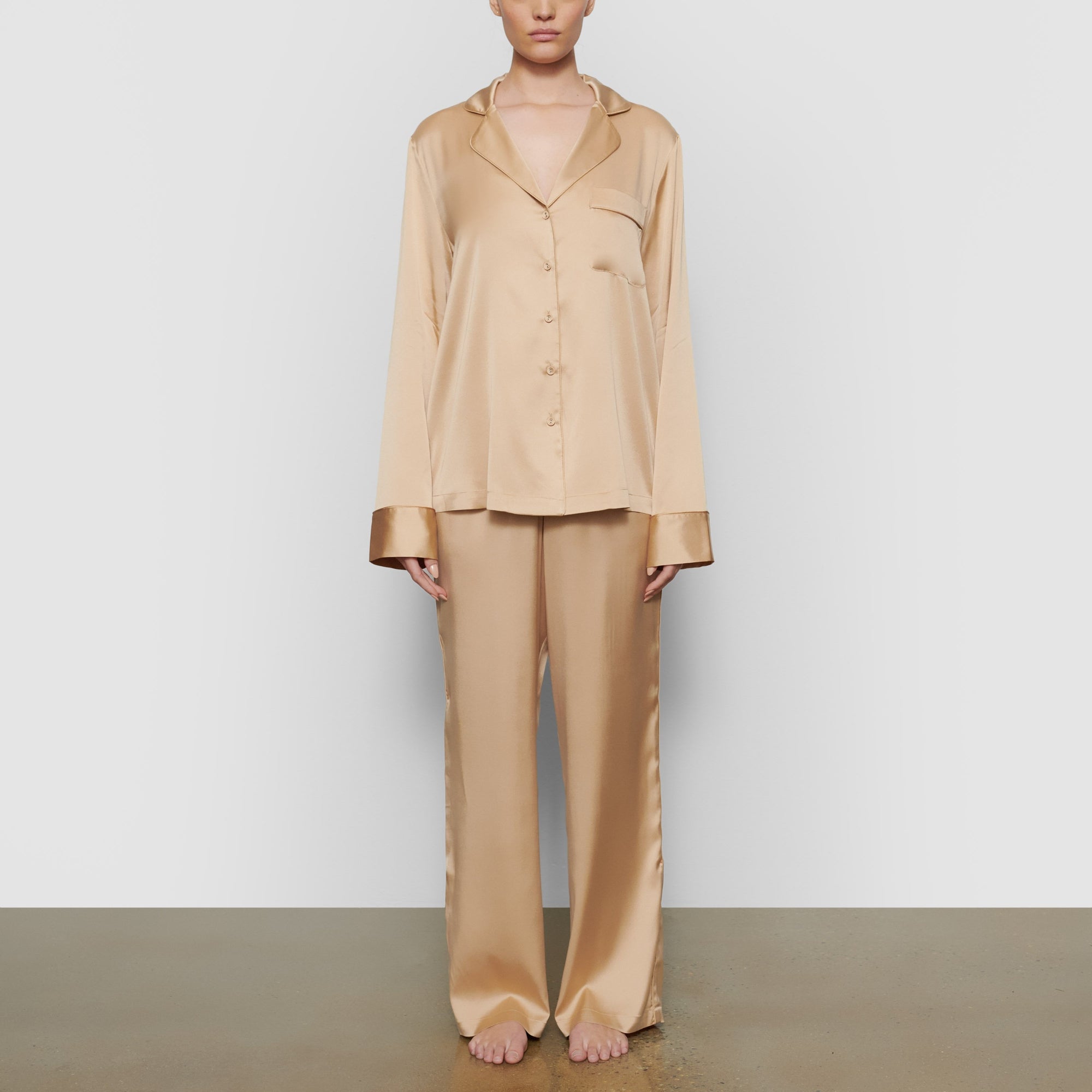 A MODEL STANDS FACING FORWARD WEARING THE SKIMS SILK BUTTON UP SHIRT IN HONEY | SEE: XXS, XS, S