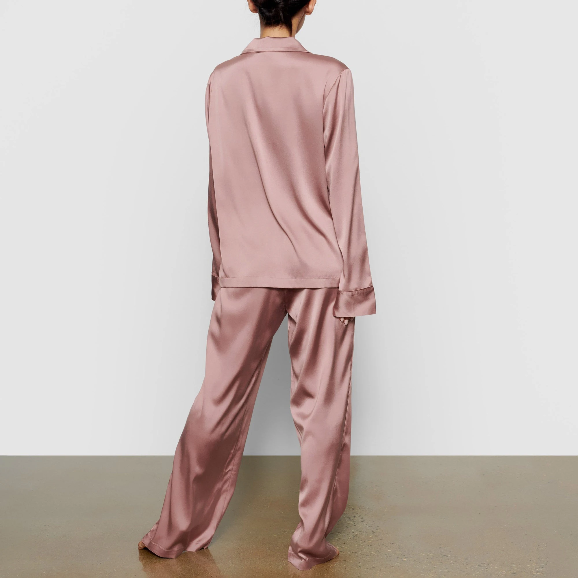 A MODEL STANDS WITH HER BACK TO THE CAMERA SHOWING THE SILK BUTTON UP SHIRT | ROSE