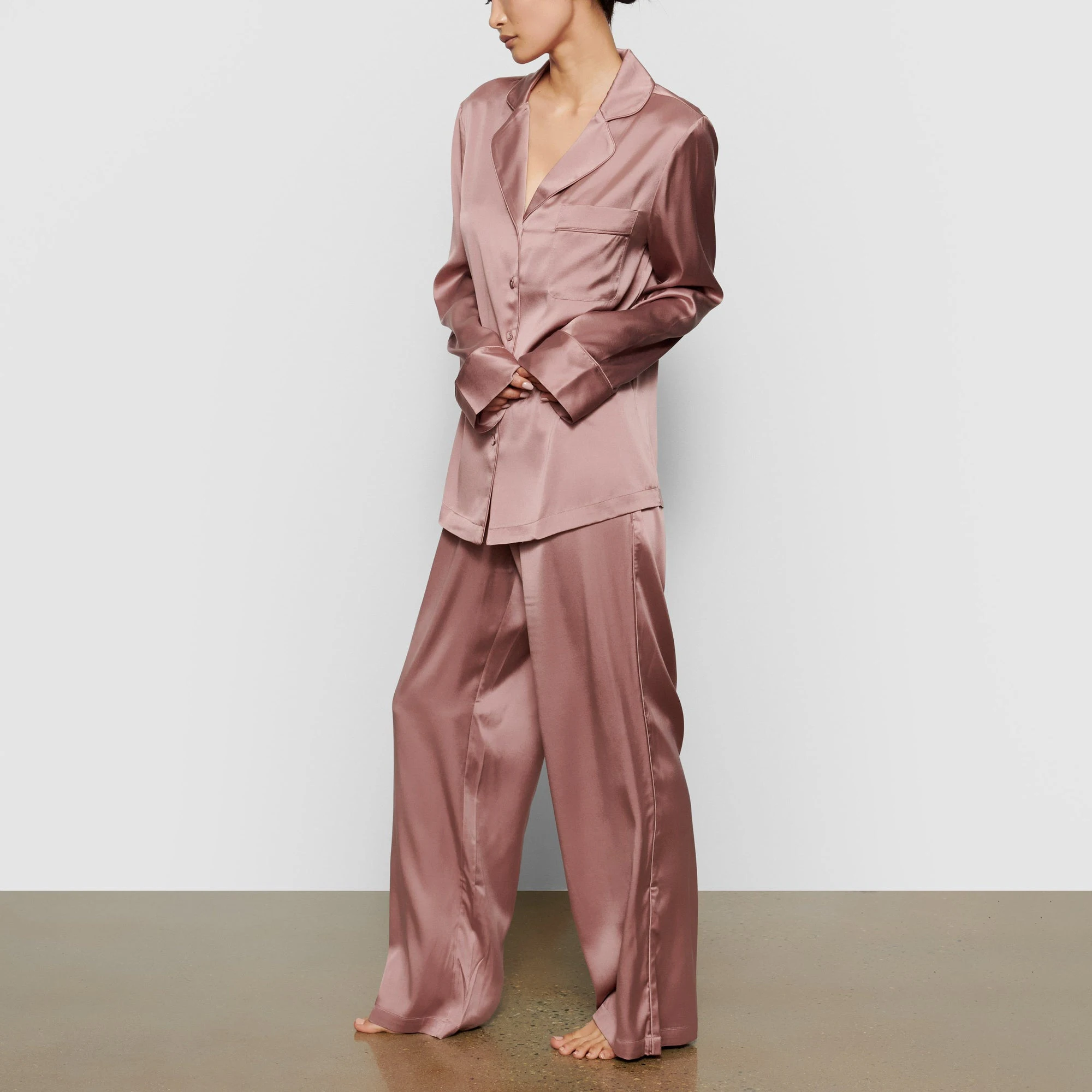 A MODEL STANDS SIDEWAYS SHOWING THE PROFILE OF THE SILK BUTTON UP SHIRT | ROSE