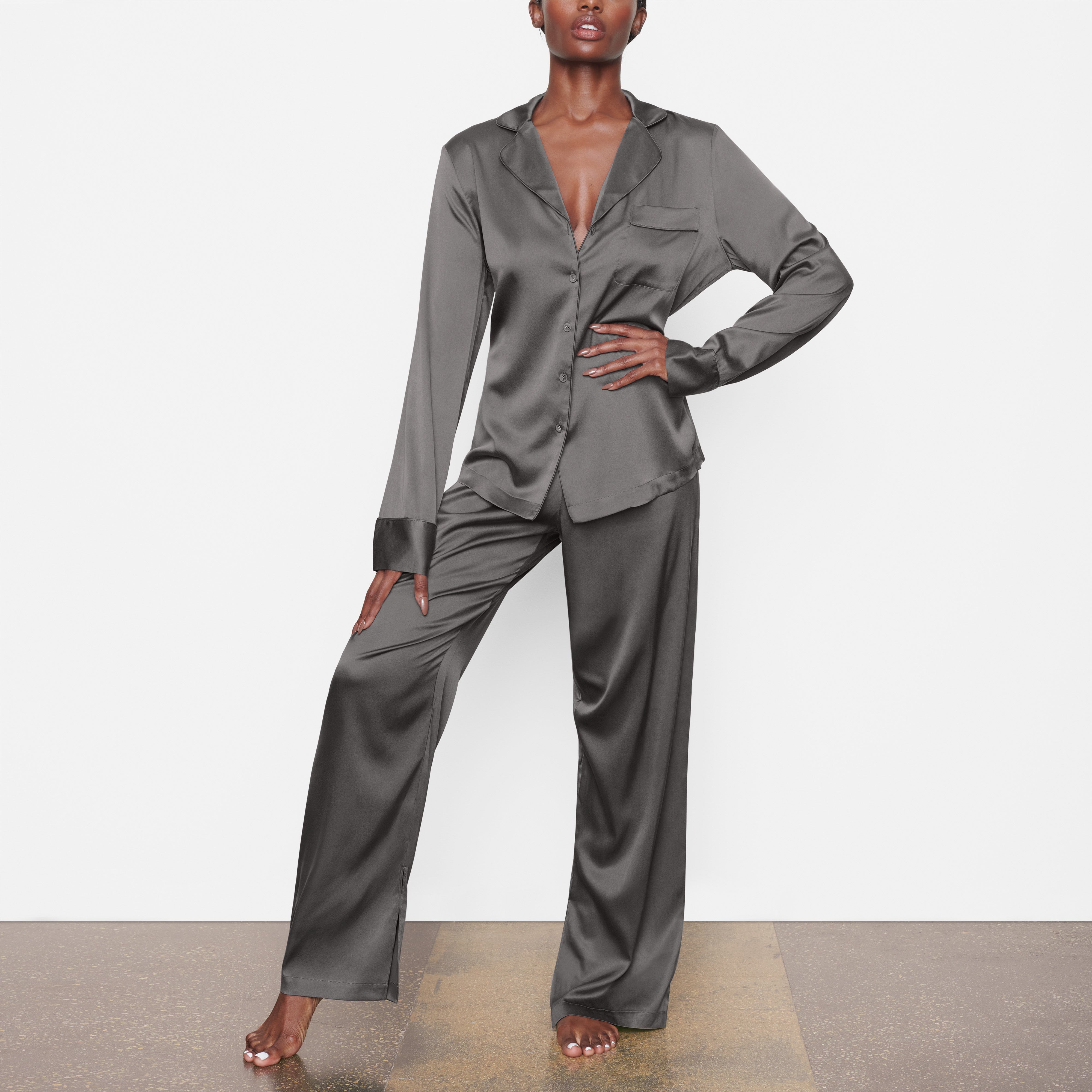 A MODEL STANDS FACING FORWARD WEARING THE SKIMS SILK BUTTON UP SHIRT IN GUNMETAL | SEE: XXS, XS, S