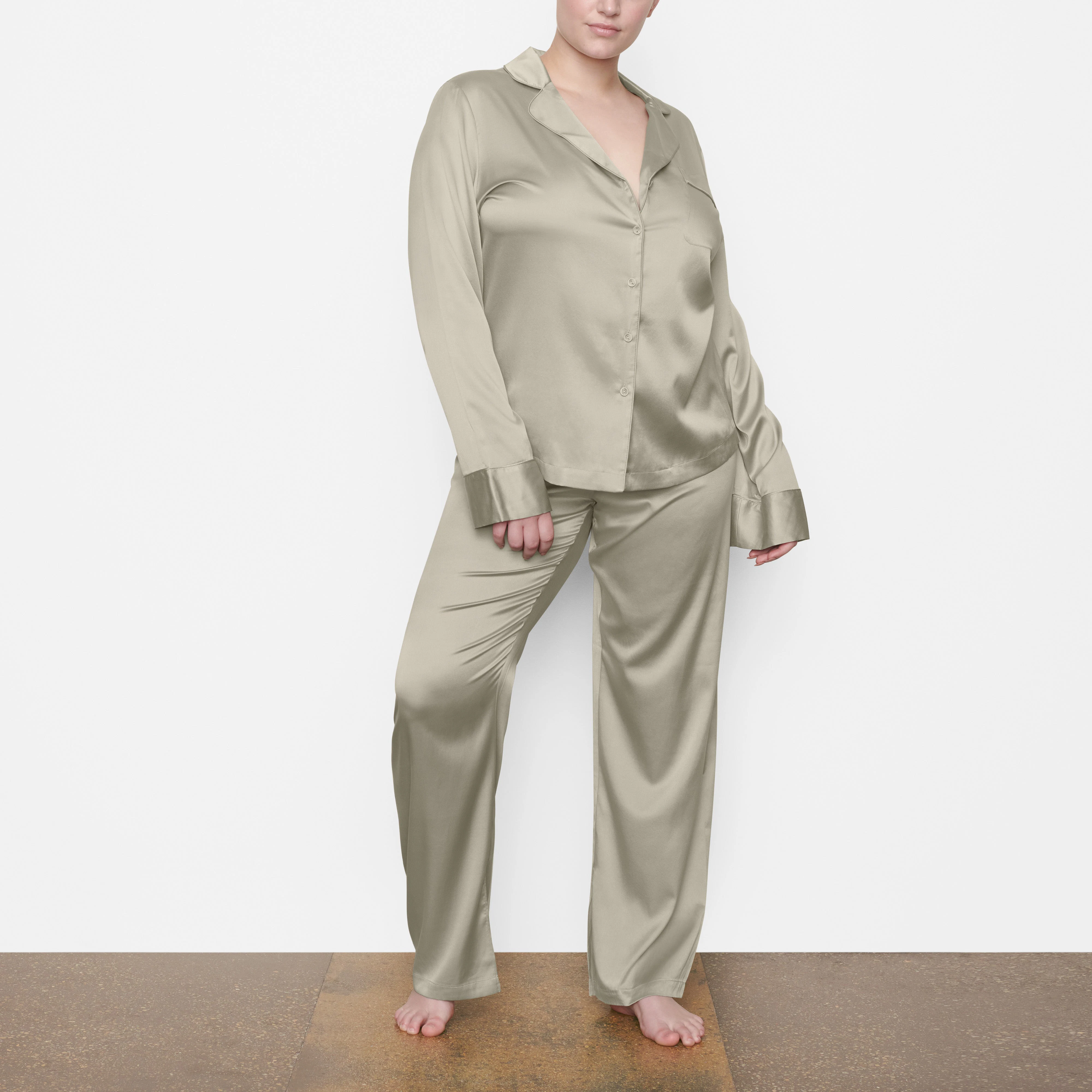 A MODEL STANDS FACING FORWARD WEARING THE SKIMS SILK BUTTON UP SHIRT IN TALC | SEE: M, L, XL