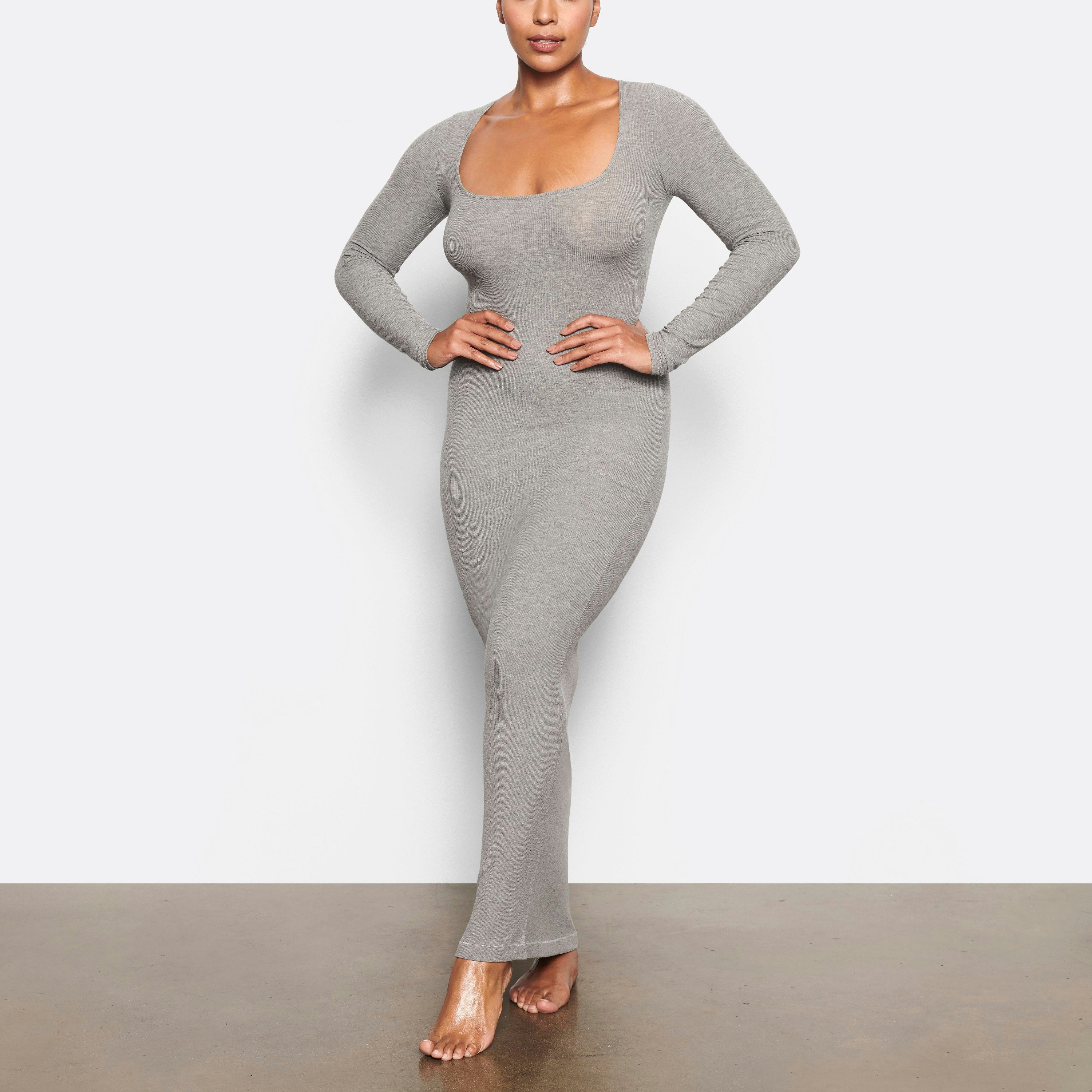 A MODEL STANDS FACING FORWARD WEARING THE SKIMS SOFT LOUNGE LONG SLEEVE DRESS IN HEATHER GREY | SEE: M, L, XL