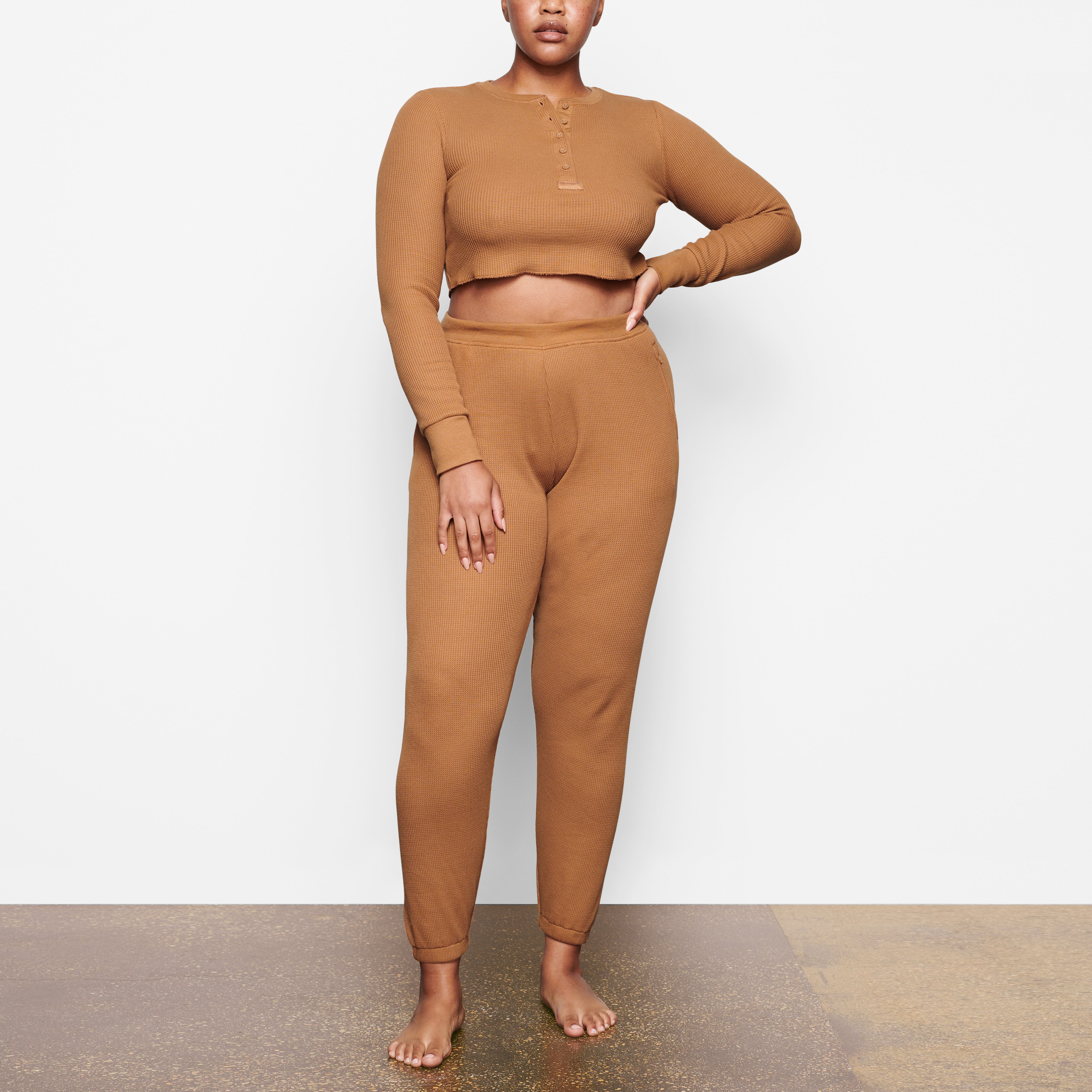 A MODEL STANDS FACING FORWARD WEARING THE SKIMS WAFFLE JOGGER IN CAMEL | SEE: M, L, XL